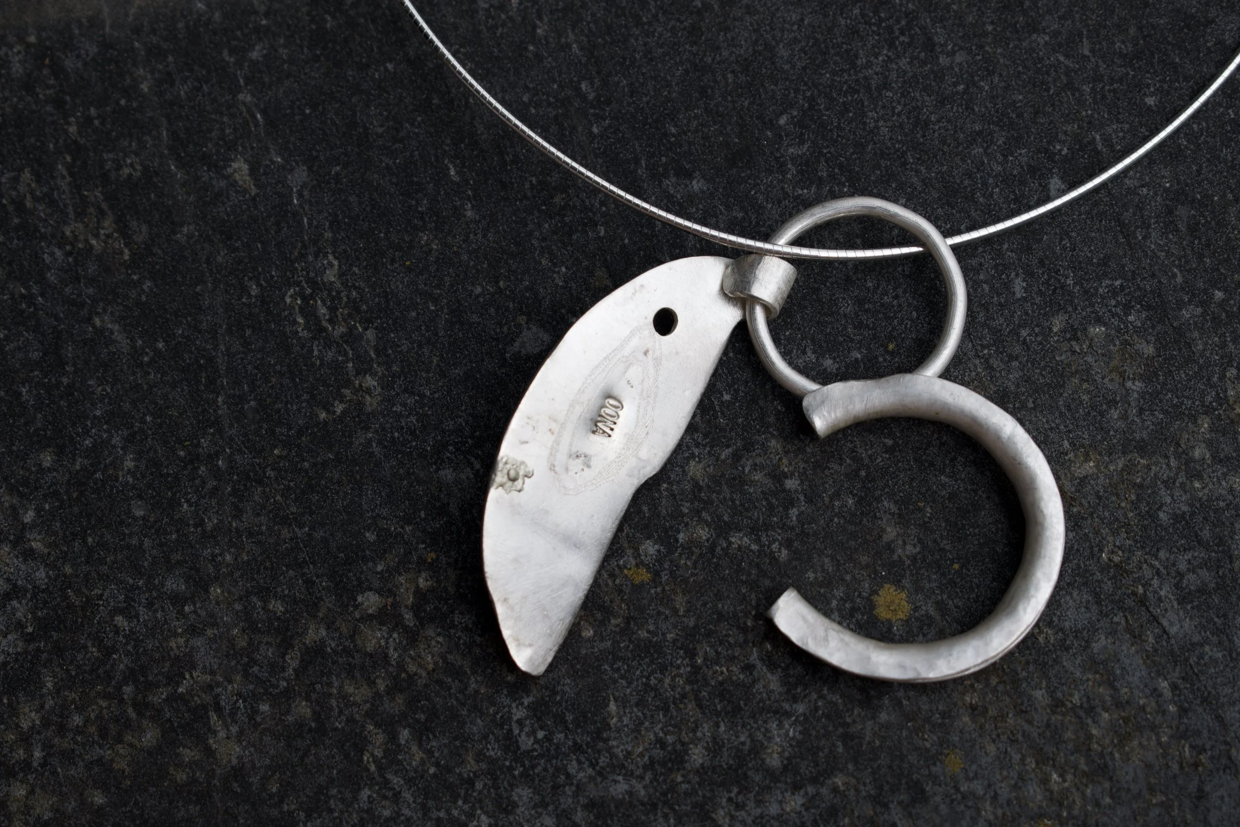 Close-up of a silver necklace with a dog tag pendant resting on a dark, textured surface.