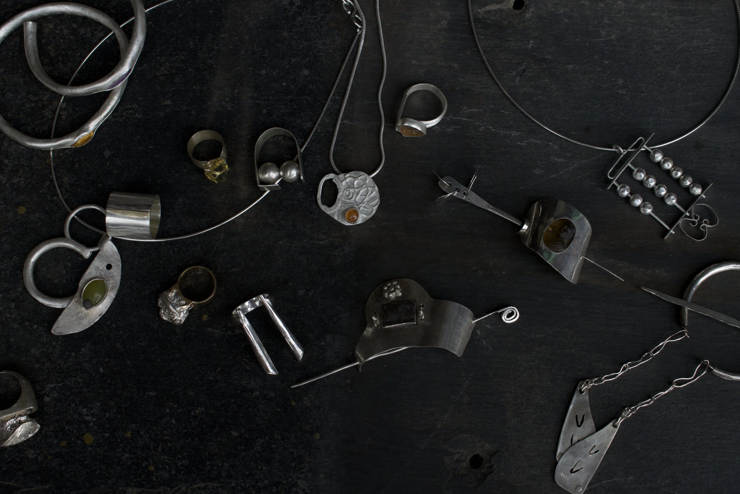 Various silver jewelry pieces including necklaces, rings, bracelets, and earrings laid out on a dark surface.