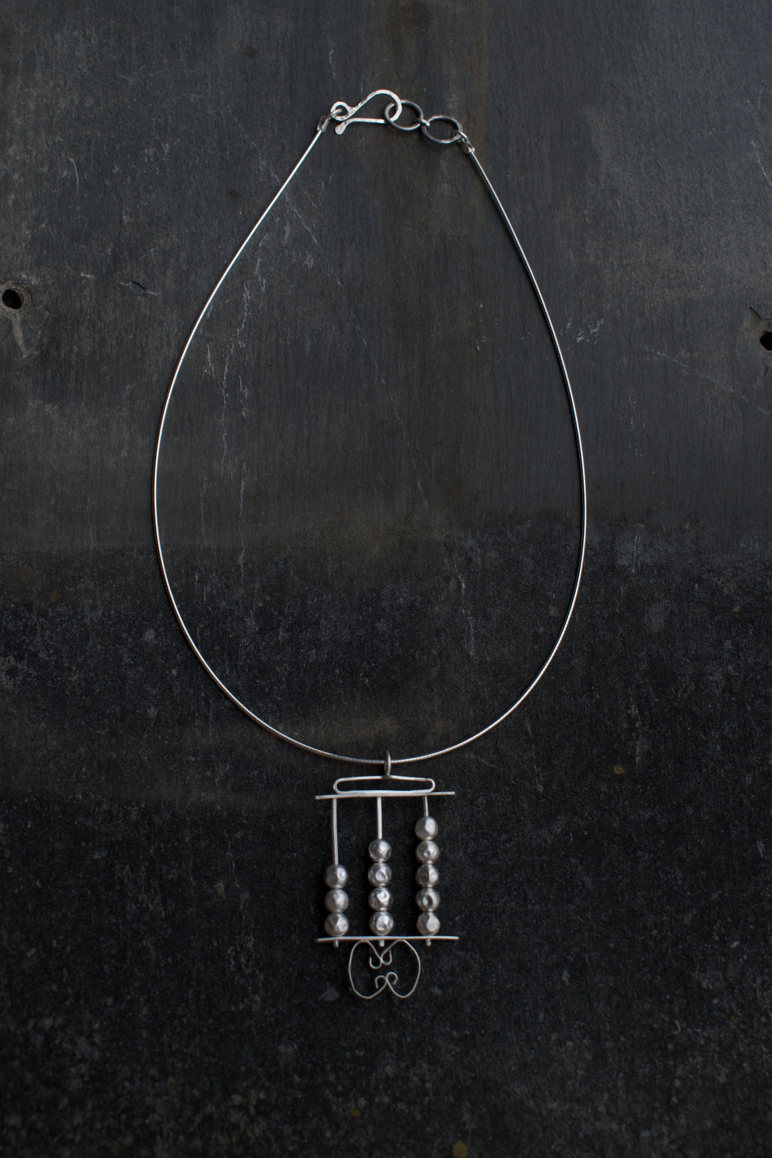 A silver necklace with pearl-like beads hanging from a decorative frame on a dark surface.