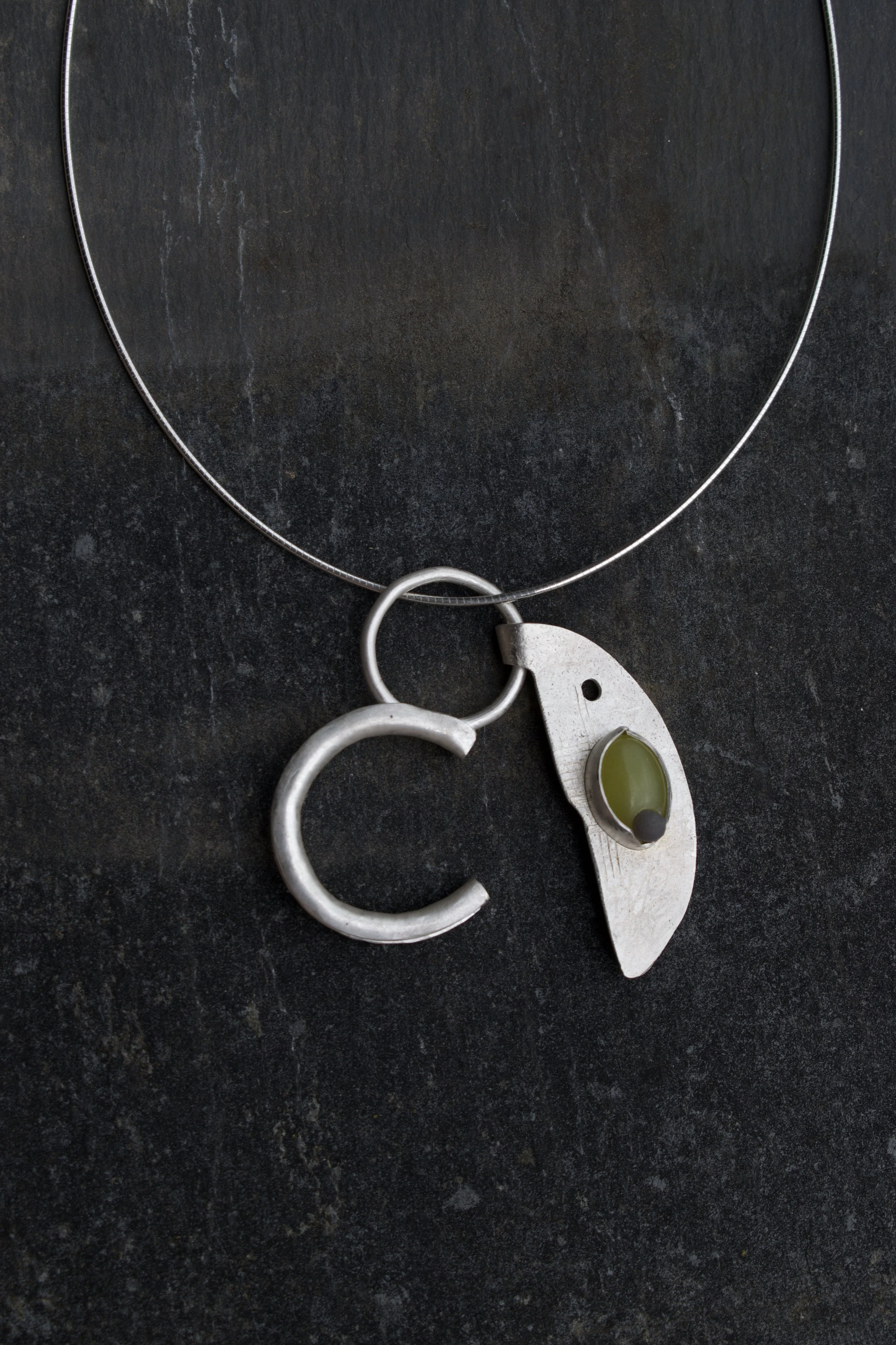 A silver necklace with a heart-shaped pendant hanging on a dark textured surface