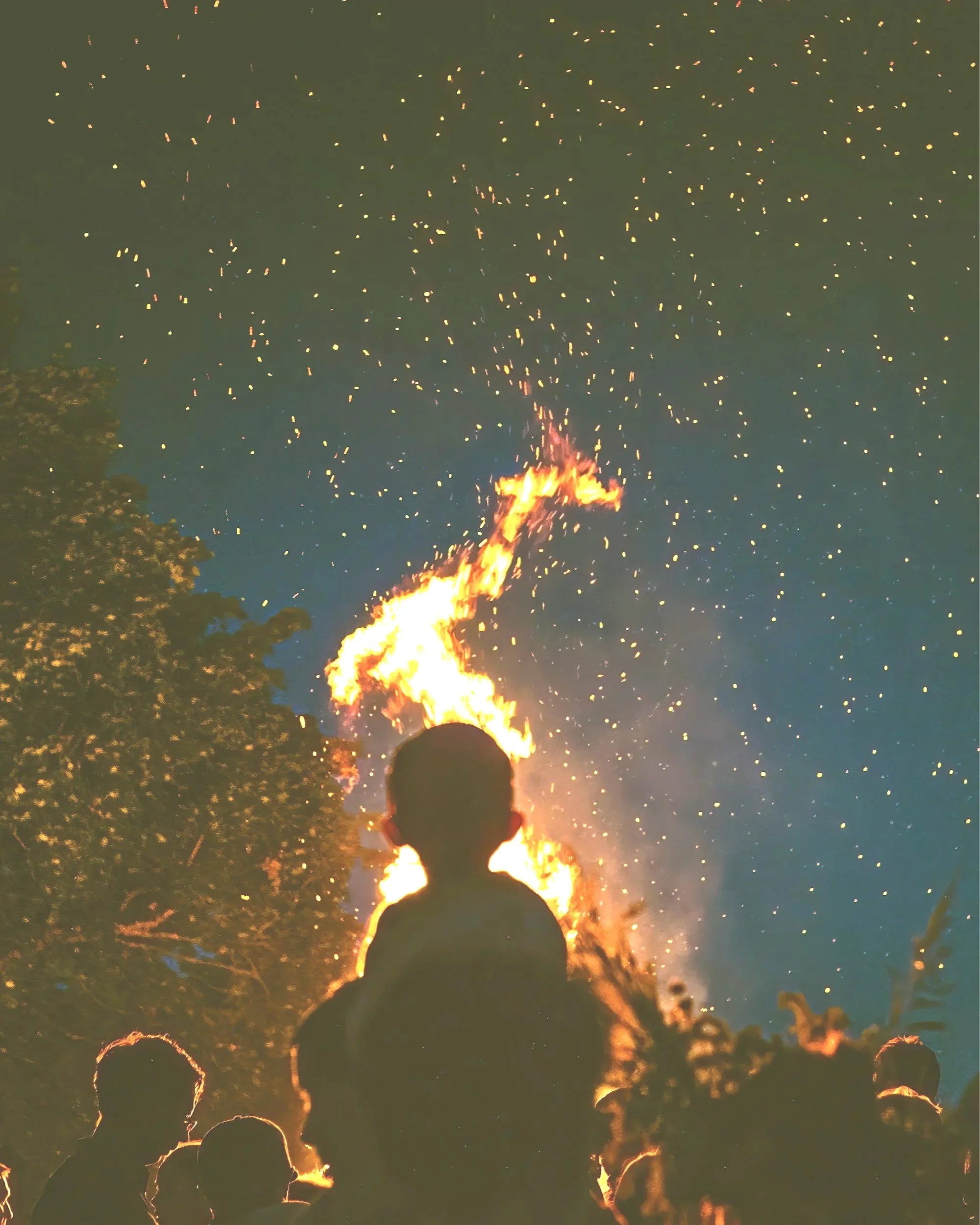 Eine Gruppe von Menschen, darunter ein Kind, schaut auf ein Feuerwerk mit Funken und Flammen am Nachthimmel.