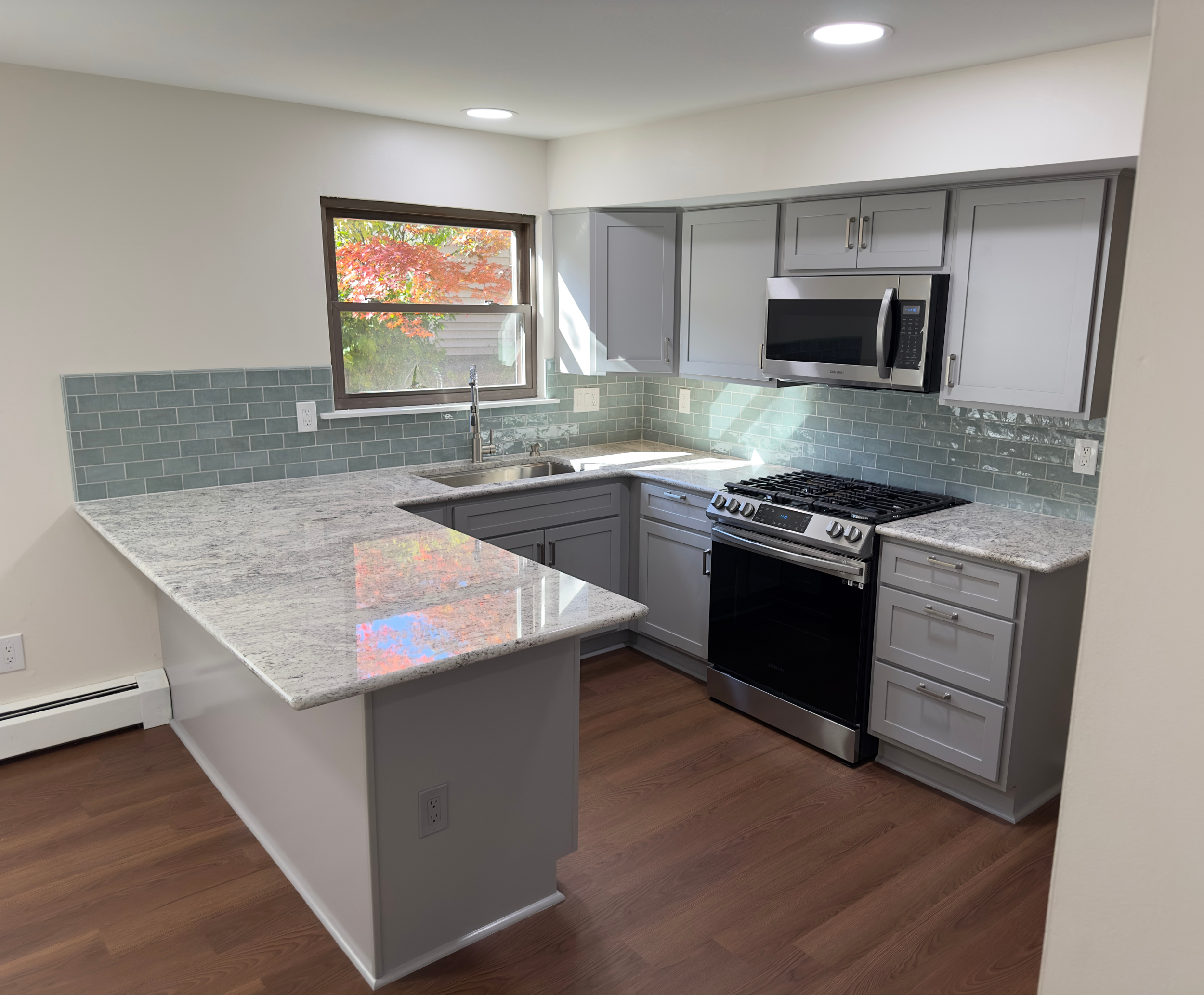 An after photo of a Glen Holman Contracting kitchen remodel with vinyl flooring, gray cabinets, and a tiled backsplash.