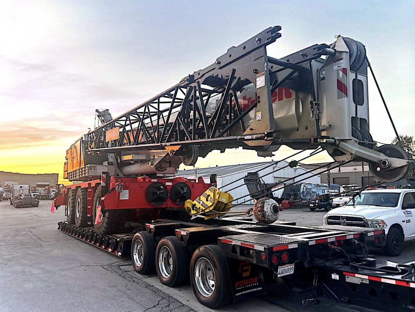 Three large trucks for transporting heavy equipment and oversized loads; the top truck has a yellow bulldozer, the middle has a covered load, and the bottom is a black semi-truck with a flatbed trailer.