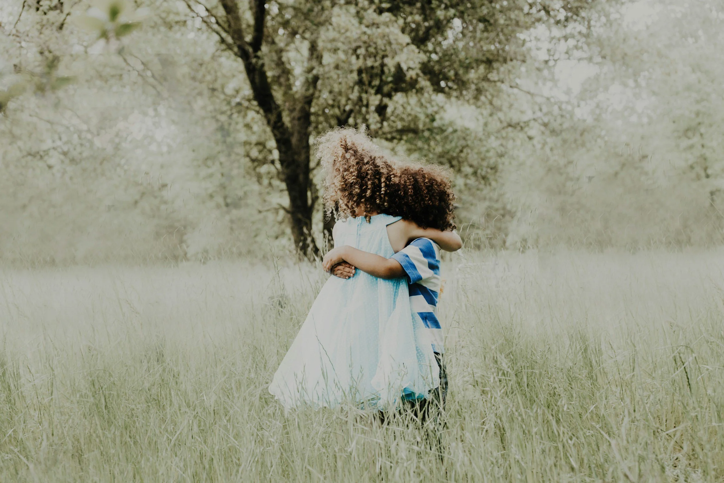 two Black children with natural, curly hair hugging in the middle of a field