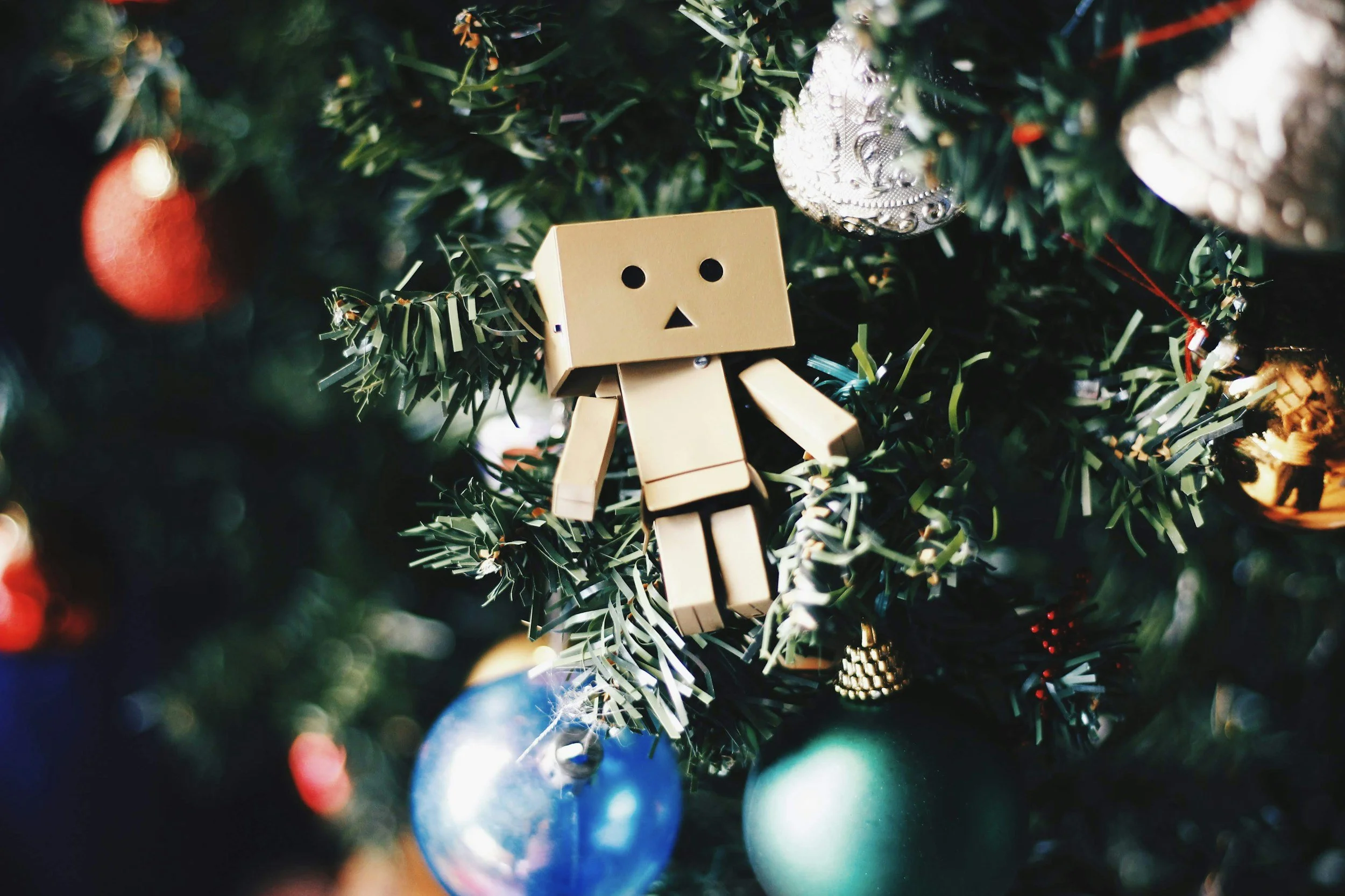 Close up of a sad block person ornament on a Christmas tree surrounded by pretty Christmas ornaments.