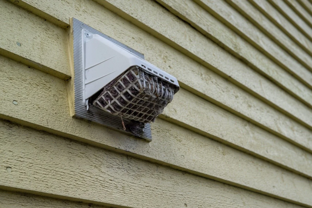 Exterior of a house with a dryer vent cover blocked with dryer lint.