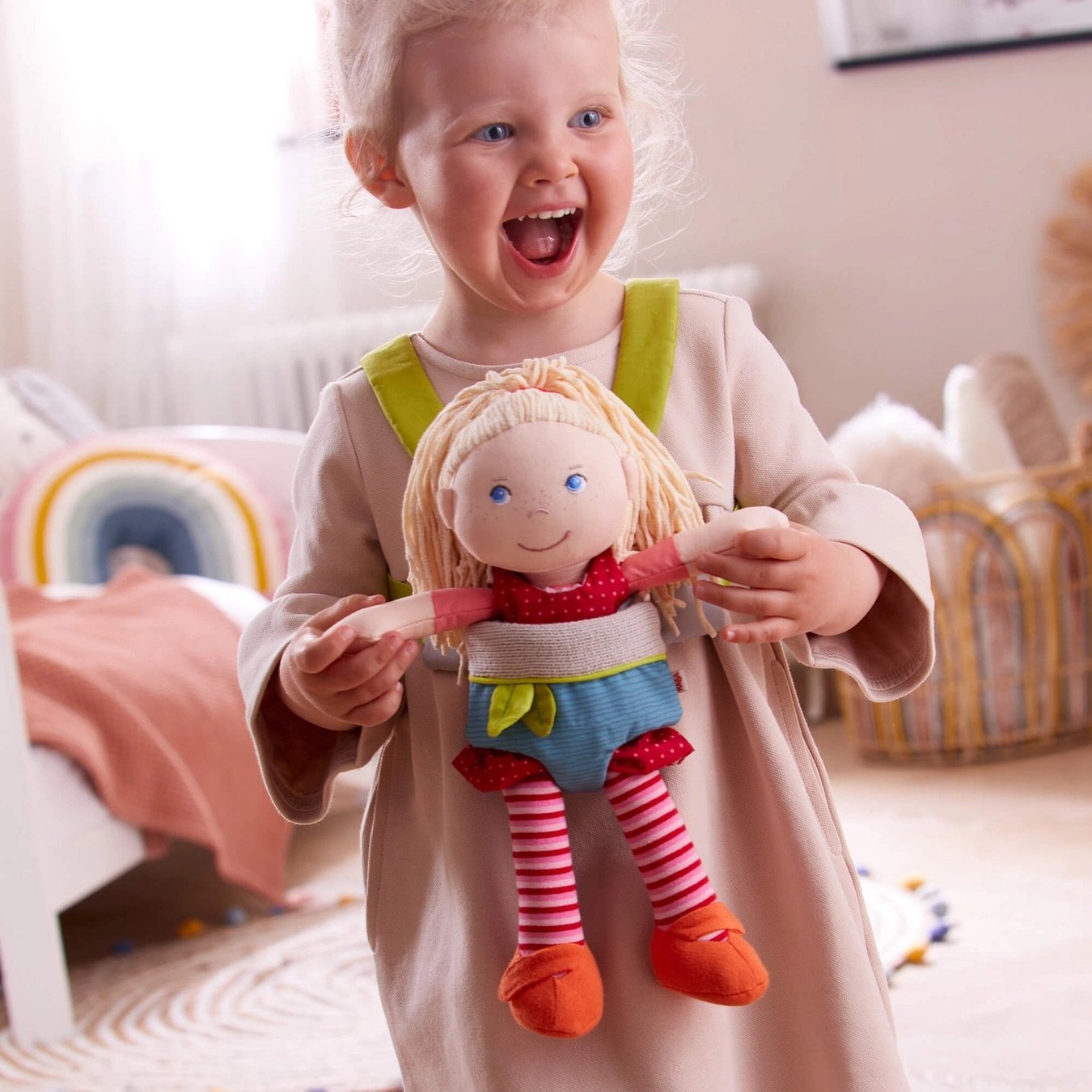 Image of a young girl in a pink dress with a plush baby doll in a toy baby carrier