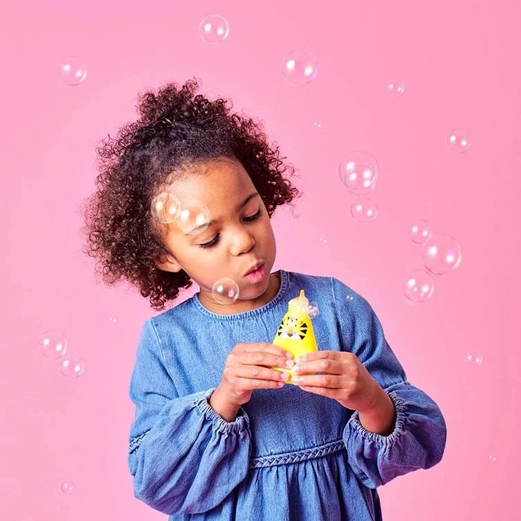 Photo of a girl blowing bubbles on a pink background