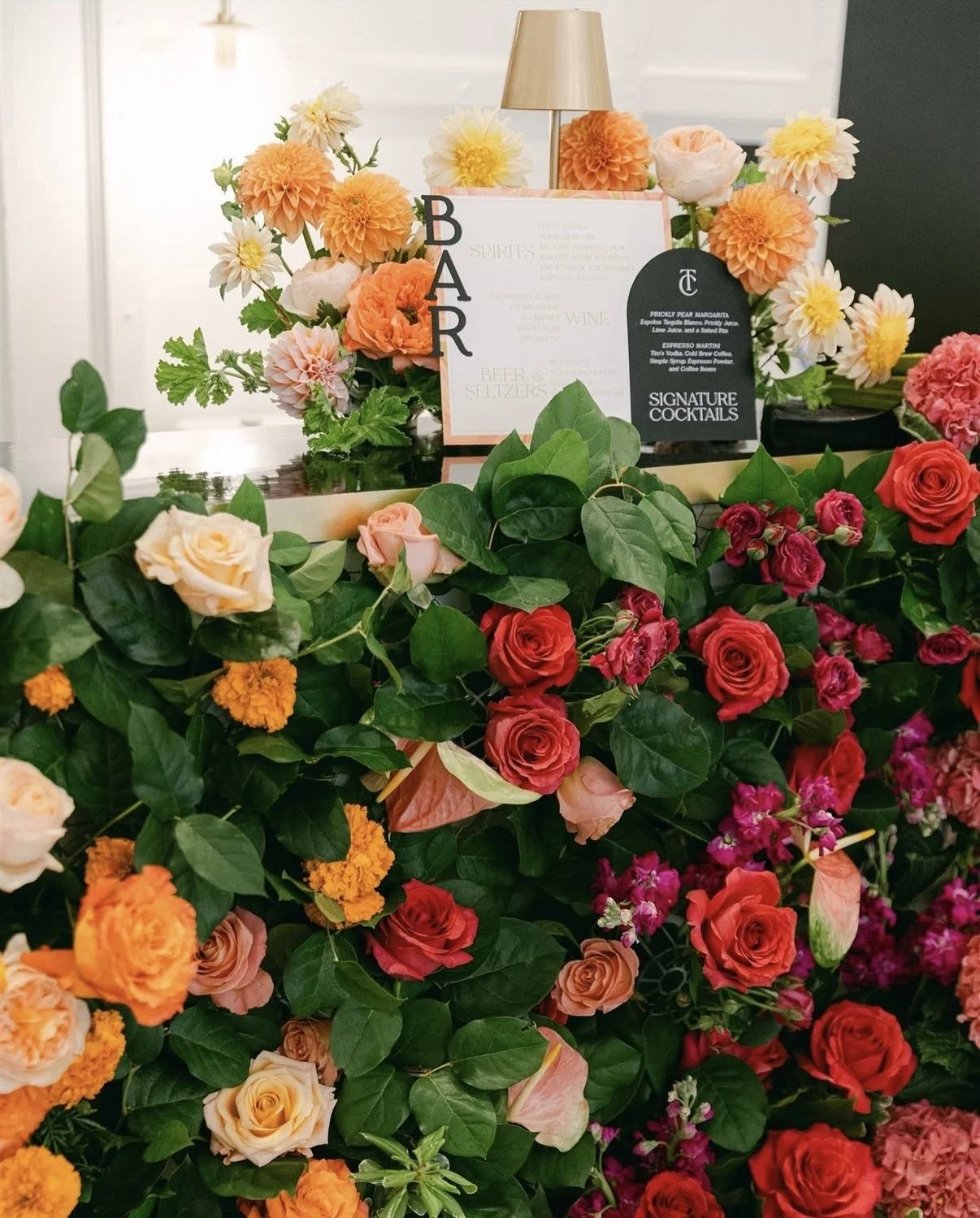 A beautifully decorated wedding reception table with an abundance of pink, purple, and white flowers, candles, and glassware, set in a modern indoor venue.