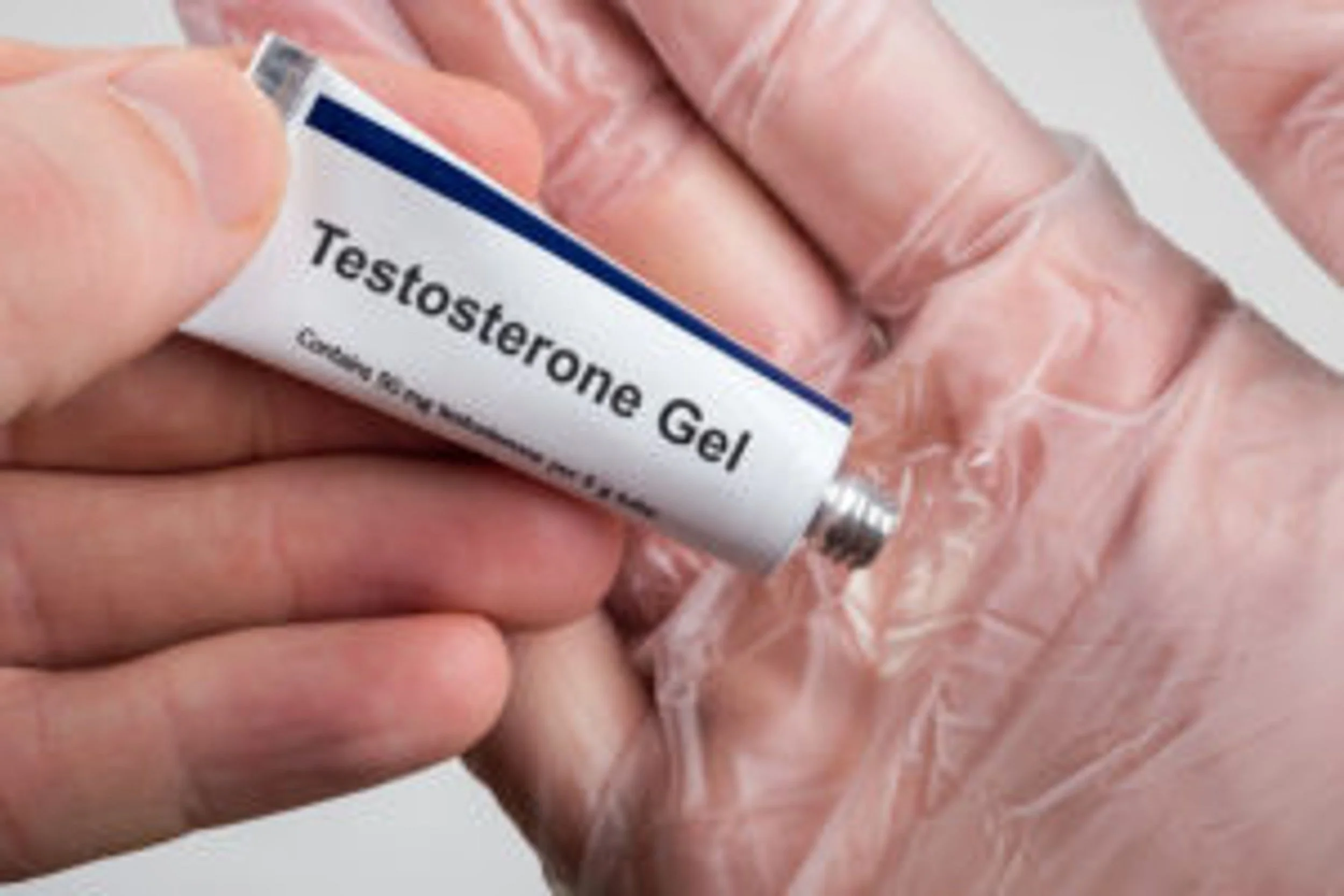 Close-up of a hand holding a small tube labeled 'Testosterone Gel'
