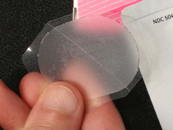 A person's hand holding a piece of protective clear film or tape, near a paper document with partially visible text.