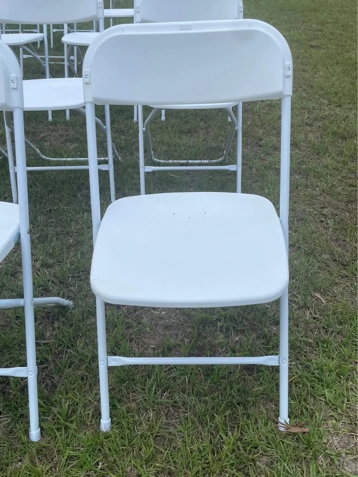 White folding chair on grass with white folding chairs in the background.