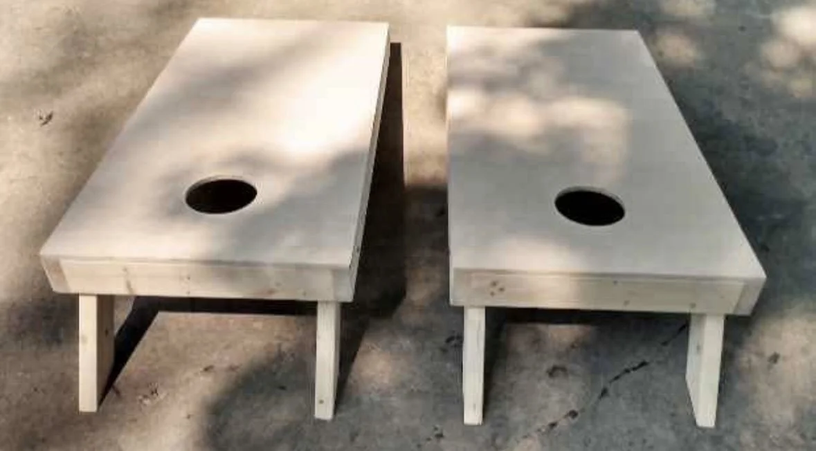 Two wooden cornhole boards with holes in the center, placed outdoors on concrete ground.