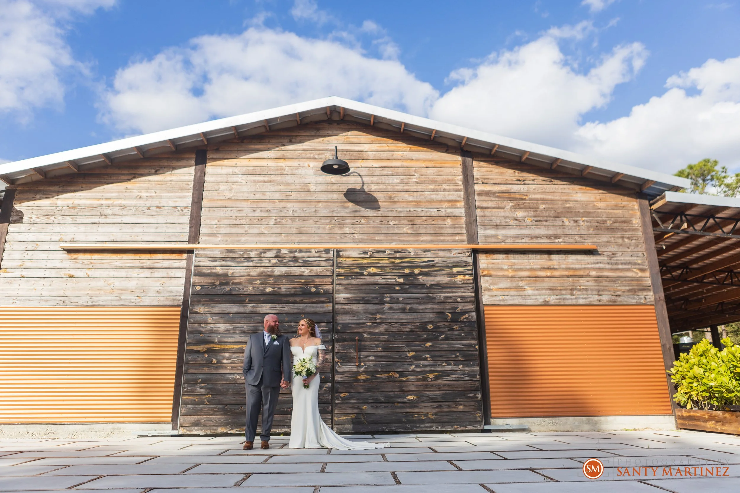 Bride and groom posing in front of a wooden building under a blue sky.