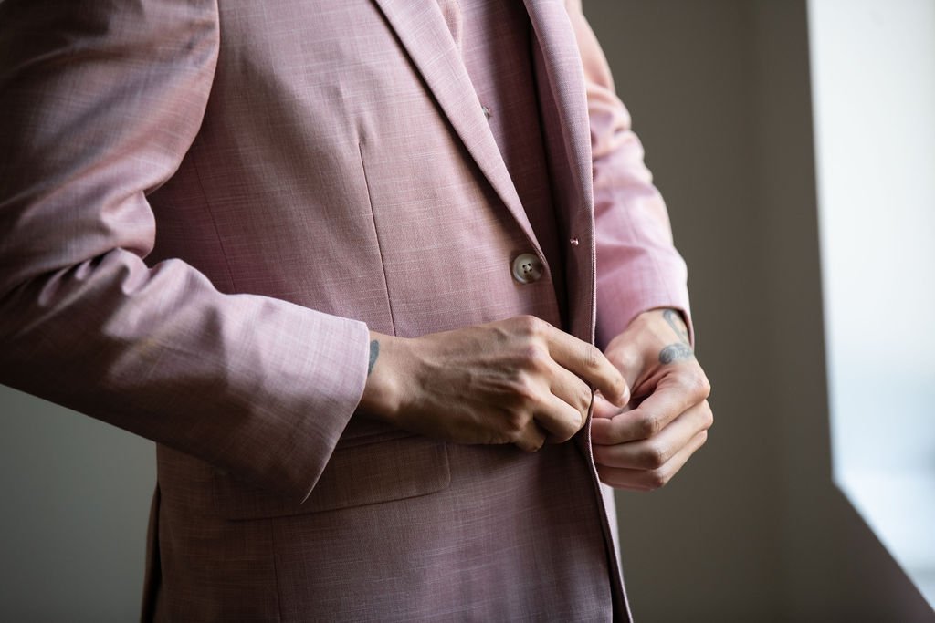 Person wearing a pink suit jacket adjusting the buttons near a window.