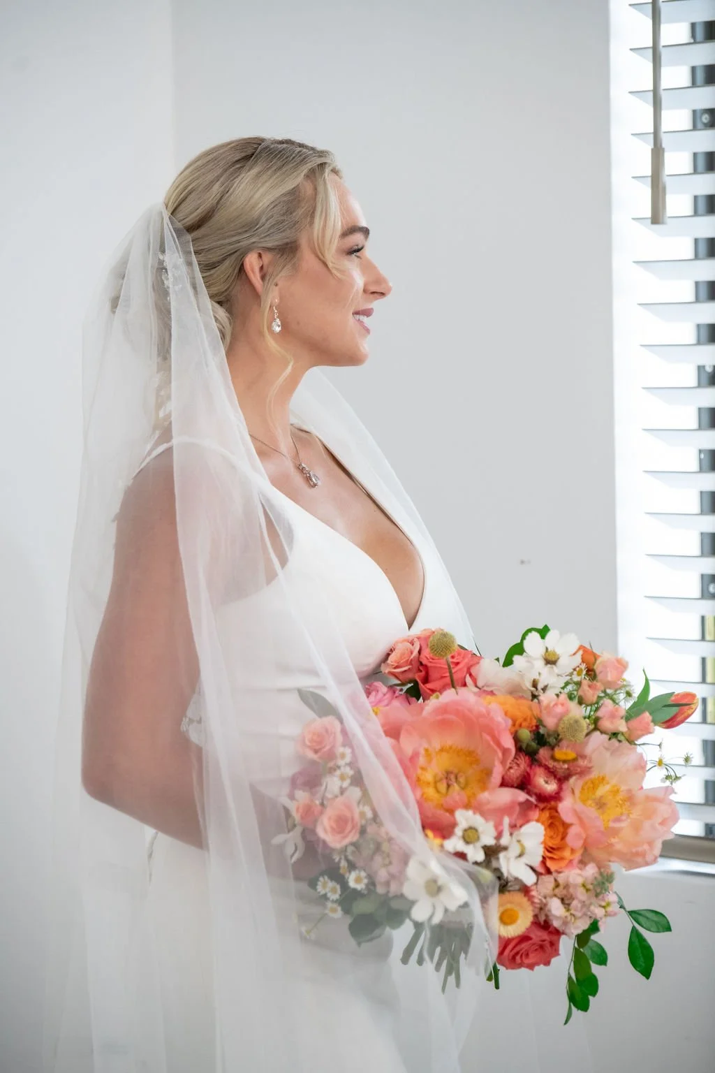 Bride in white dress with veil holding a vibrant bouquet of flowers, including pink peonies and roses.