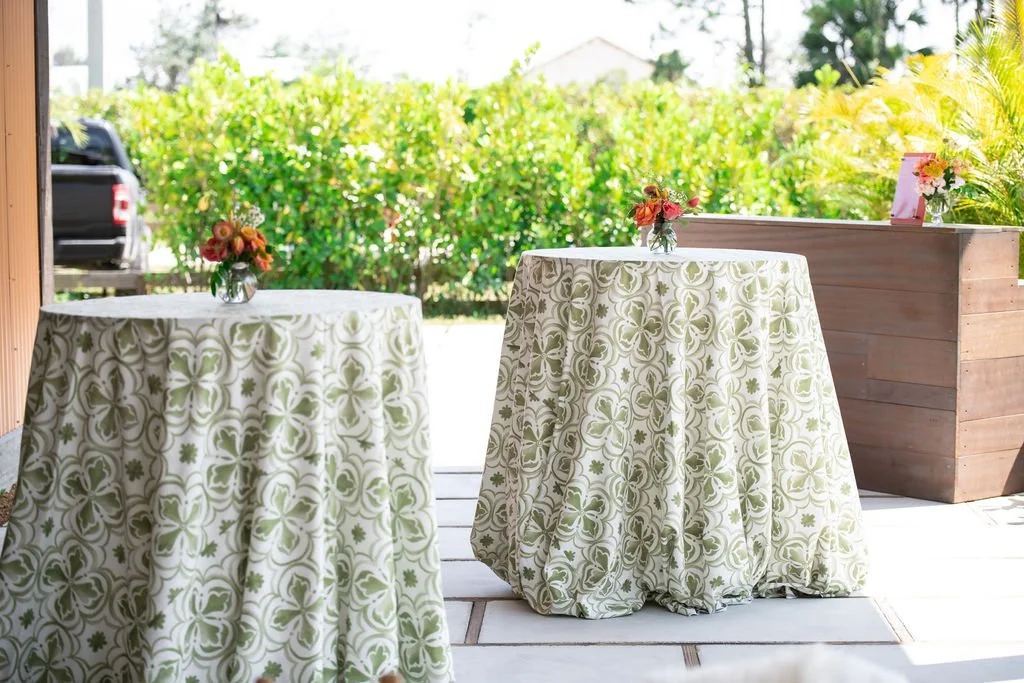 Two round tables with floral-patterned tablecloths and small flower vases on an outdoor patio.