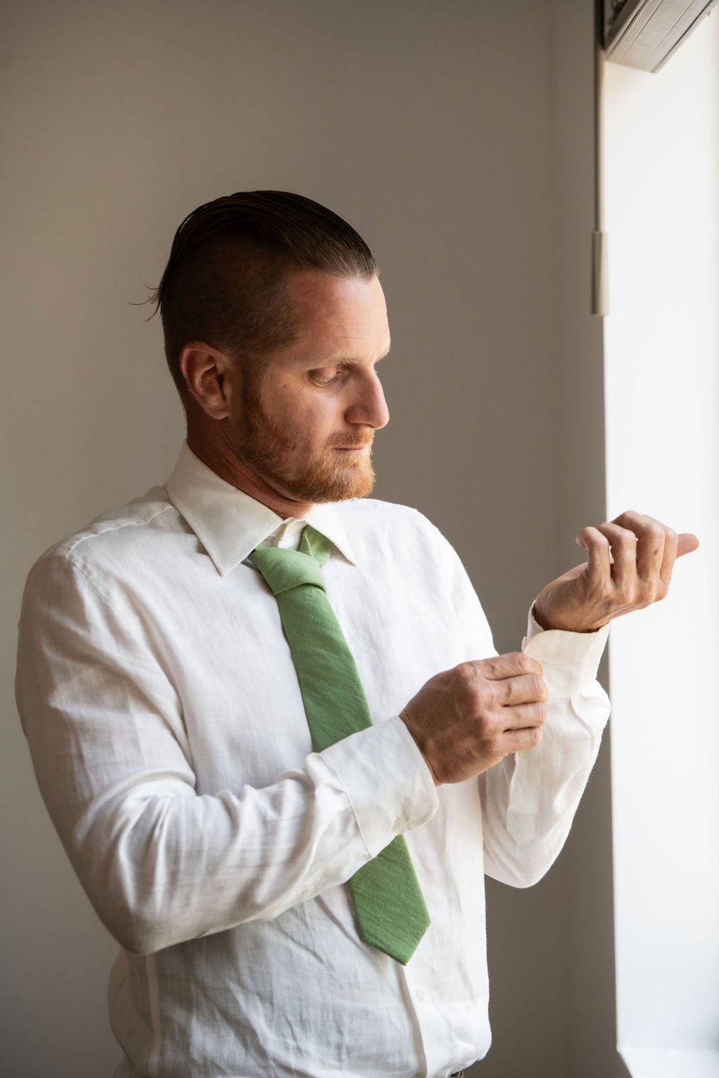 Man in a white shirt and green tie adjusting his cufflinks