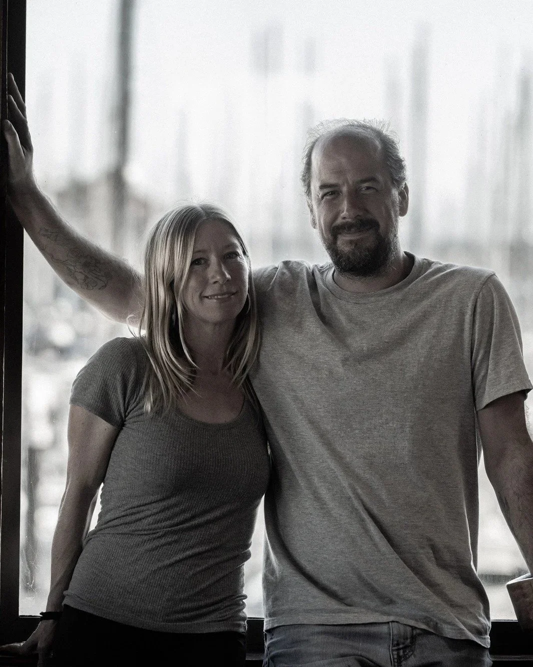 Two people, a woman and a man, standing close together by a window, smiling at the camera at Johnnys harborside restaurant.