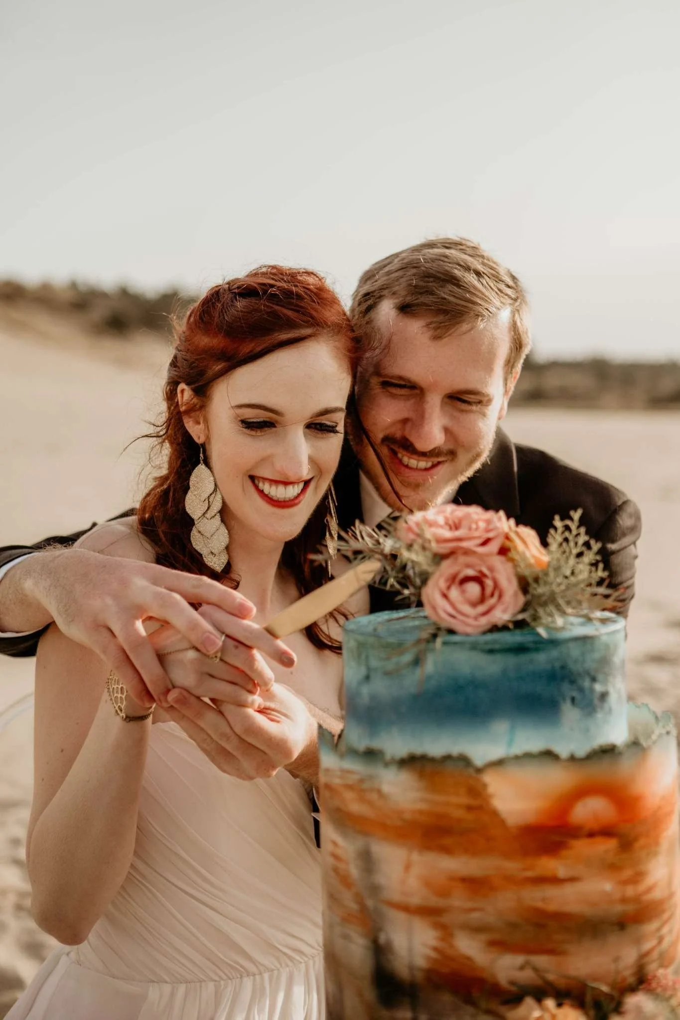 couple in the oregon sanddunes elopement cutting tiered wedding cake.jpg