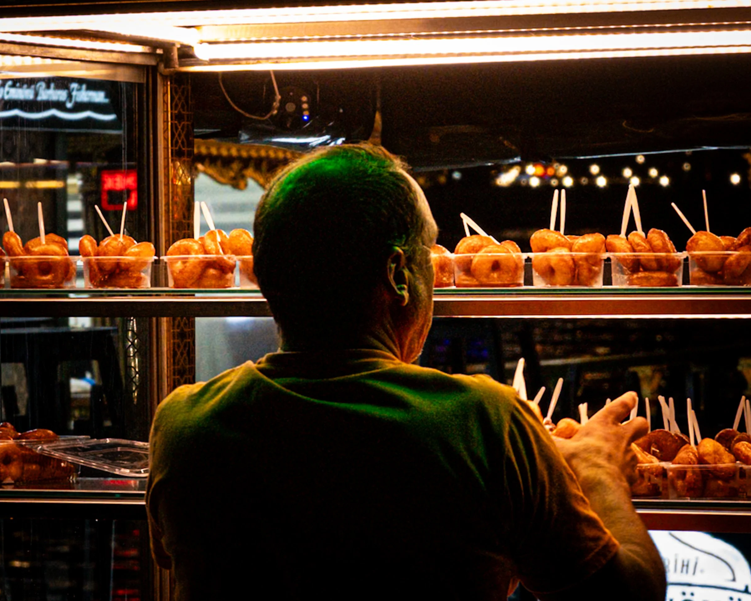 Street vendor arranging trays of lokma, traditional Turkish fried sweets, under warm lights at a food stall near the waterfront in Istanbul — vibrant night-time Istanbul street photography highlighting local food culture.