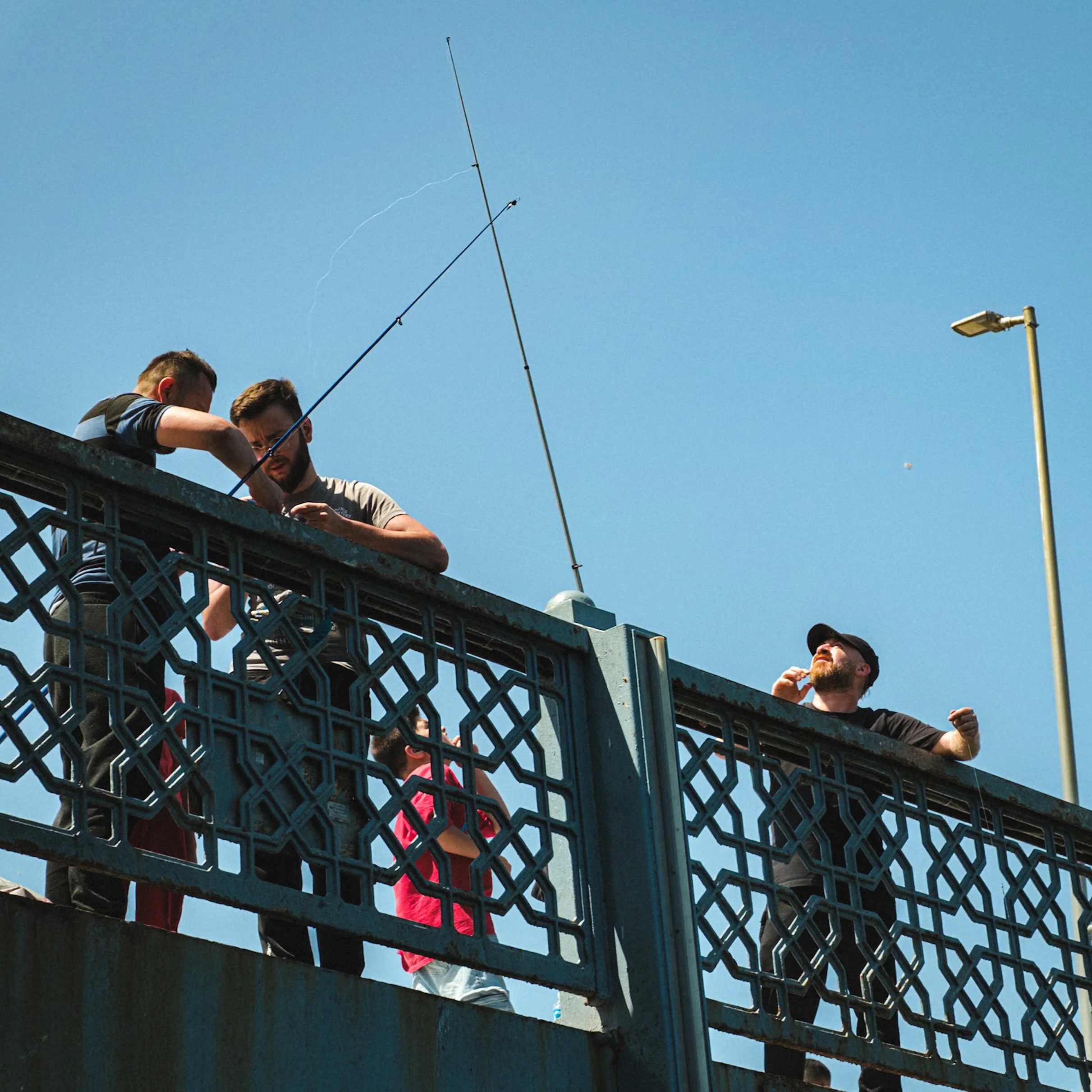 Group of men fishing from the top level of the Galata Bridge in Istanbul, with fishing rods raised against a clear blue sky — classic Istanbul street photography capturing local daily routines.