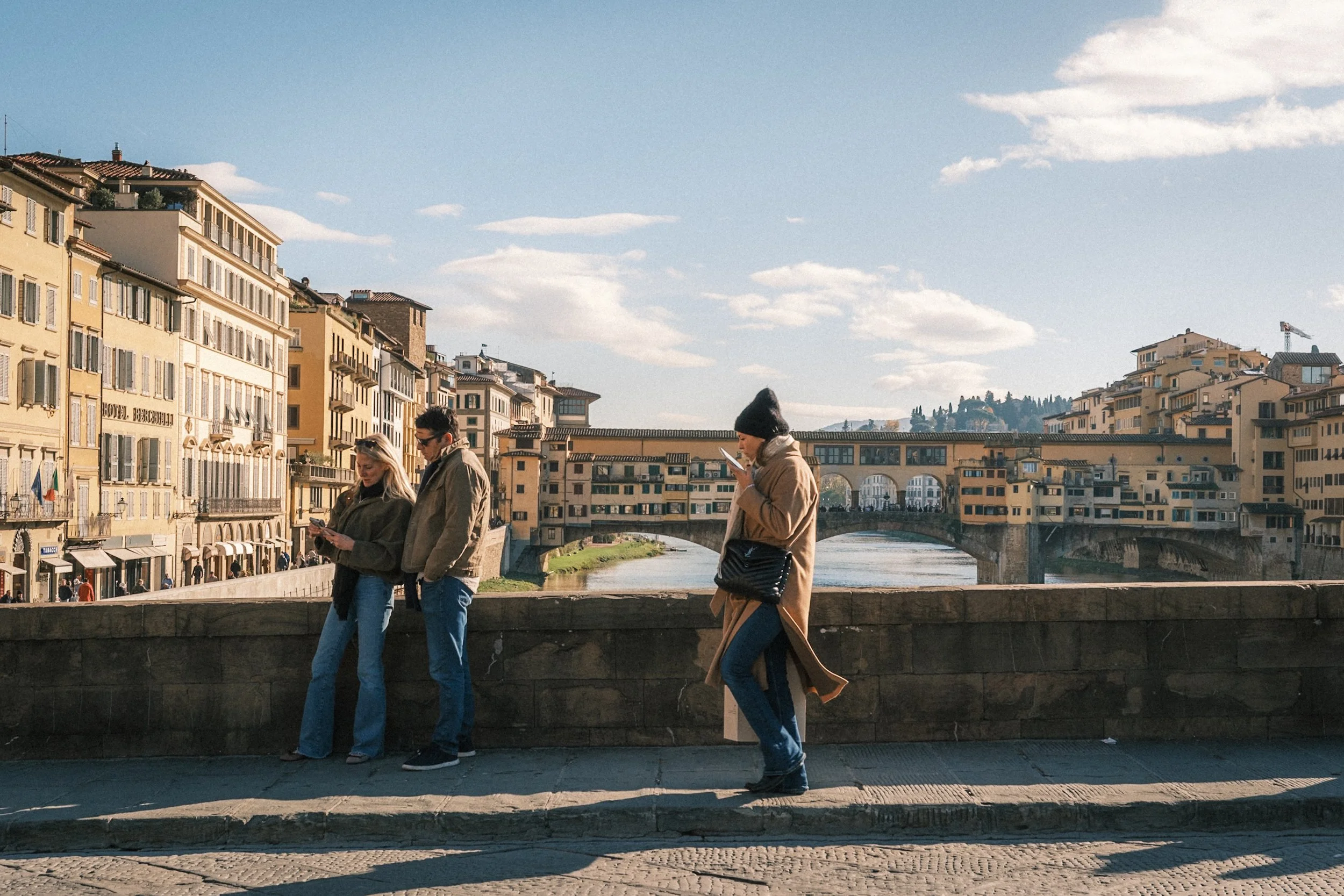 People walking beside the Arno River with Ponte Vecchio in the background