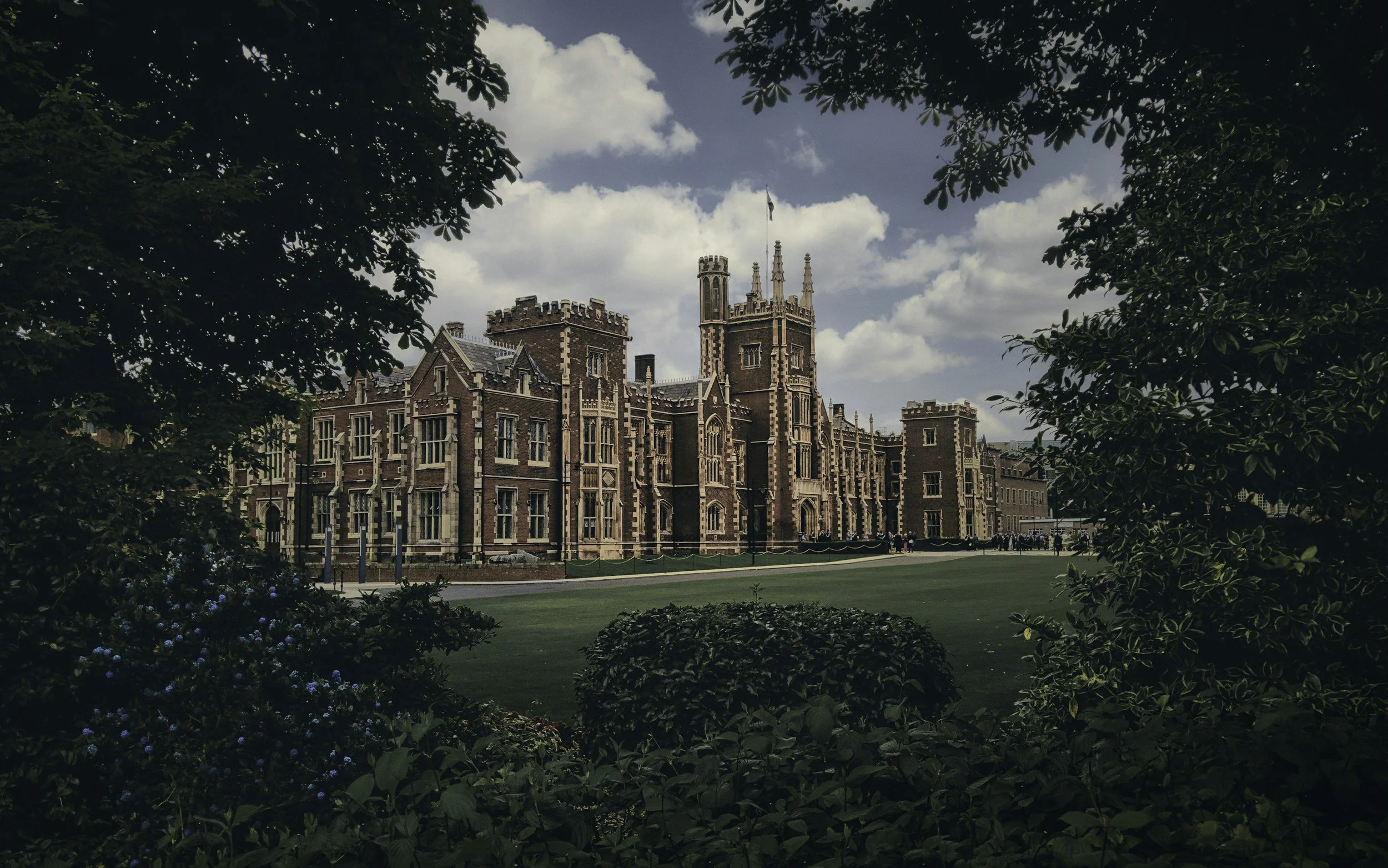 A large, historic castle-like building with turrets and gothic architecture surrounded by trees and greenery.