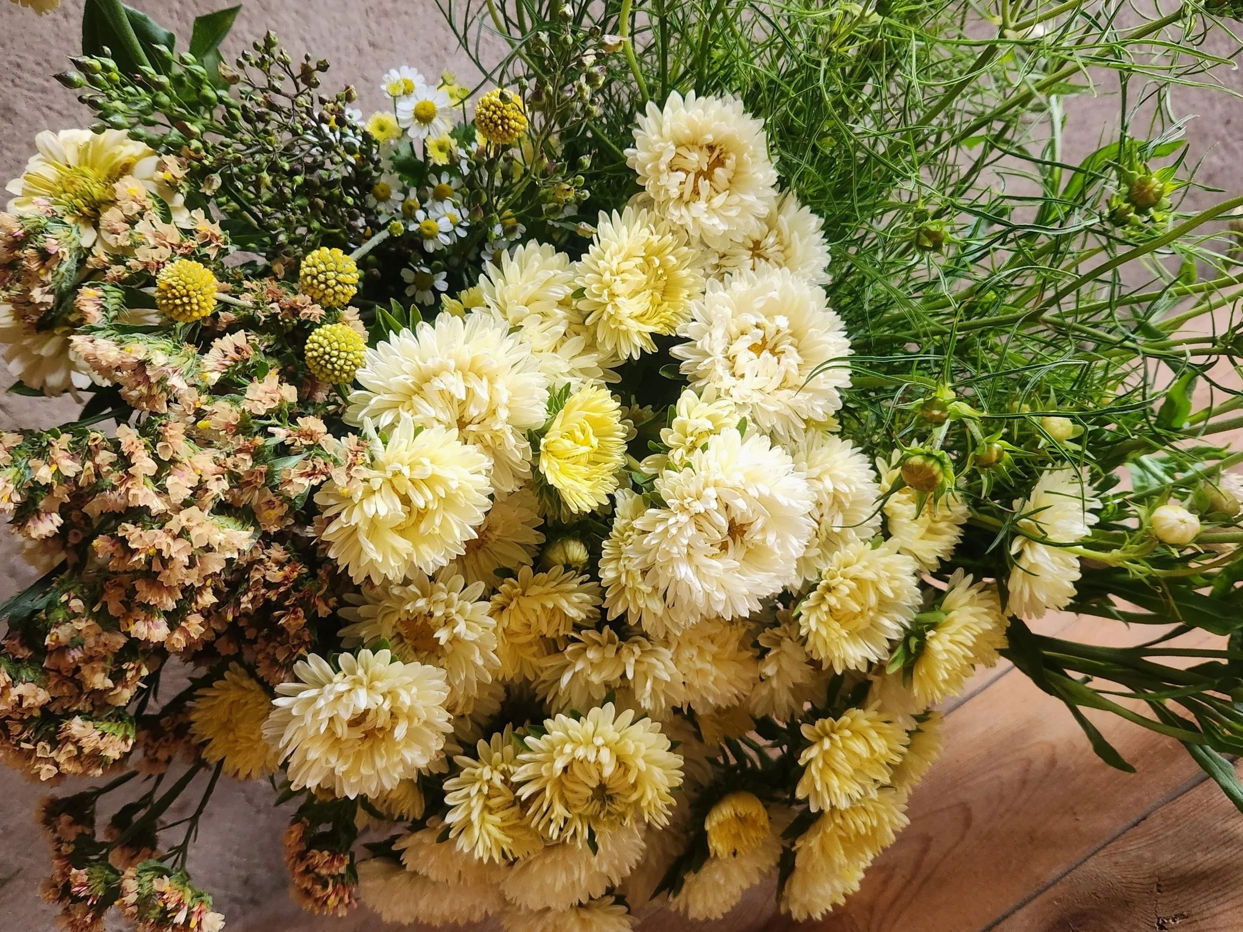 A bouquet of cream and white flowers with various green foliage on a wooden surface.