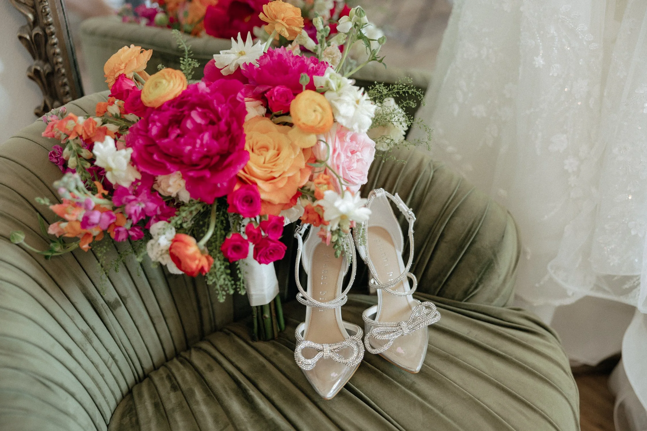 Colorful wedding bouquet and jeweled bridal shoes on a green velvet chaise lounge