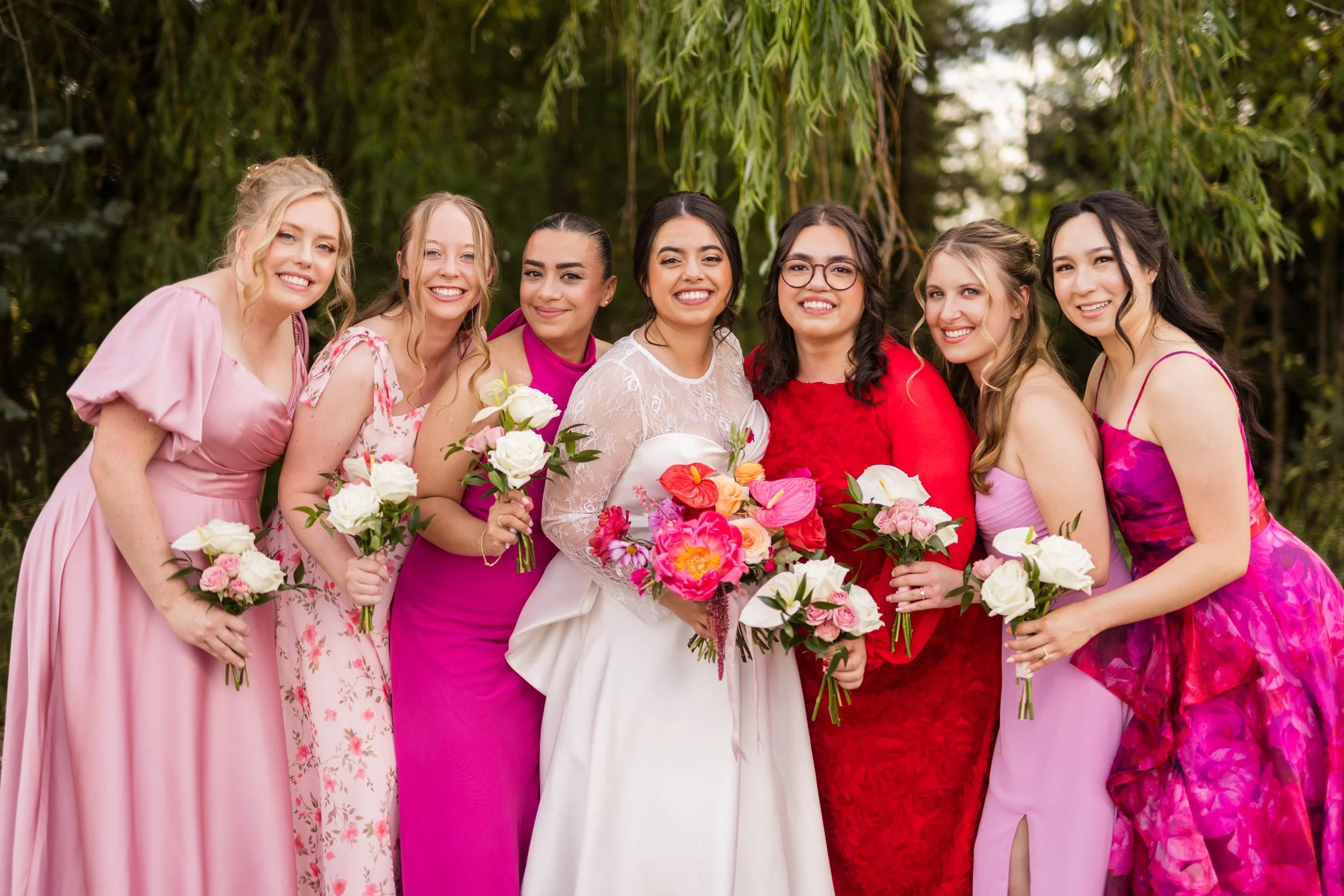 Bride and six bridesmaids holding colorful bouquets at an outdoor wedding