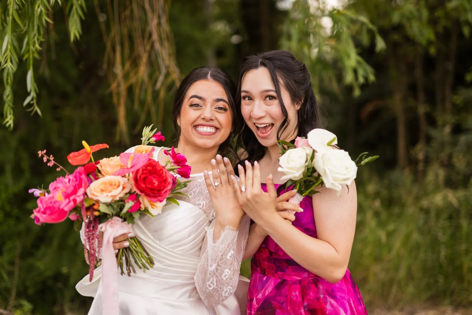 Smiling bride and bridesmaid holding colorful flower bouquets outdoors