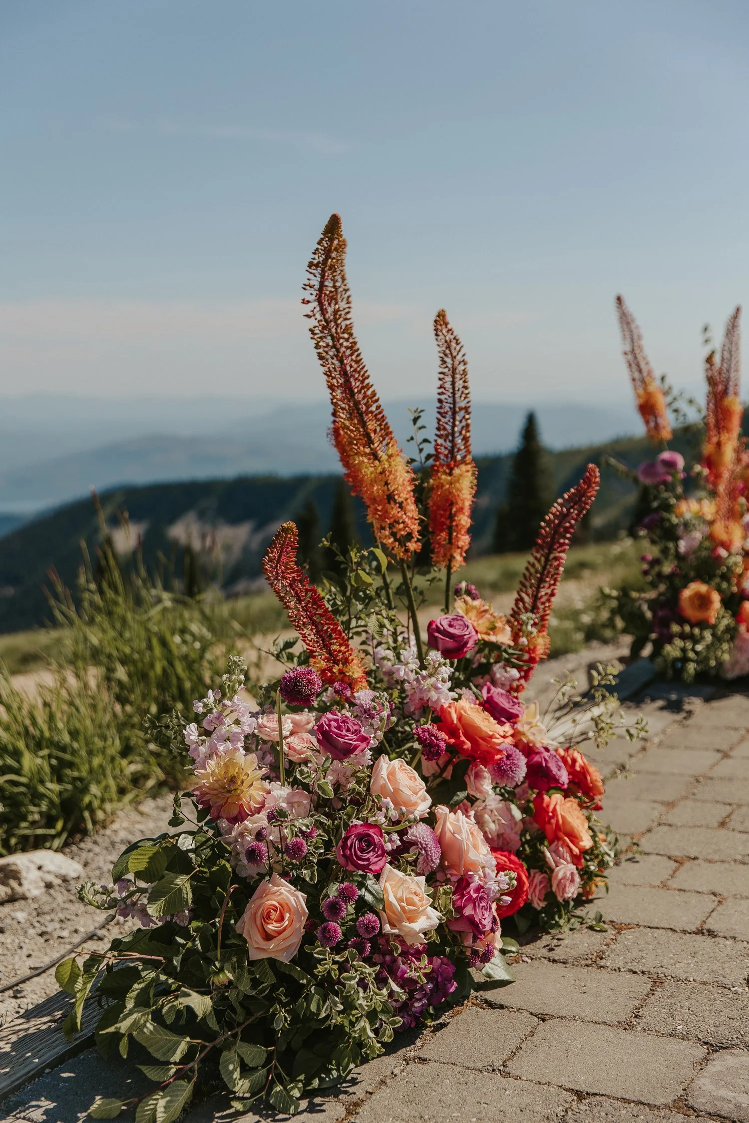 Colorful floral arrangements with roses and wildflowers lining a mountain overlook walkway