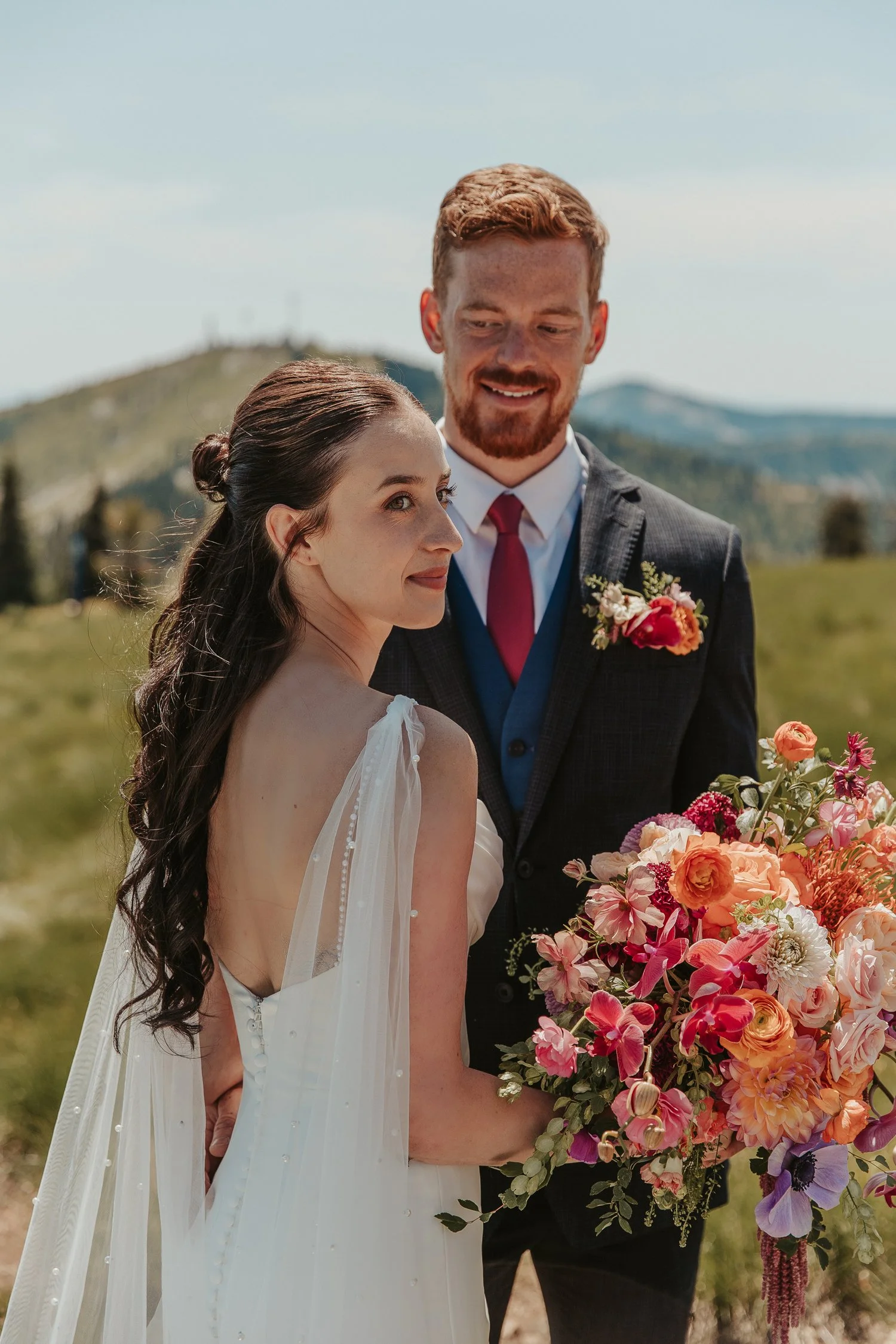 Bride and groom posing outdoors in a mountain landscape with a colorful wedding bouquet