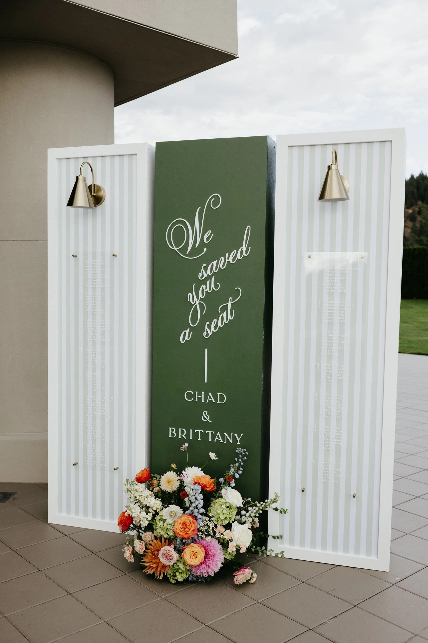 Elegant wedding seating chart display for Chad and Brittany with floral arrangement, striped panels, and brass wall sconces