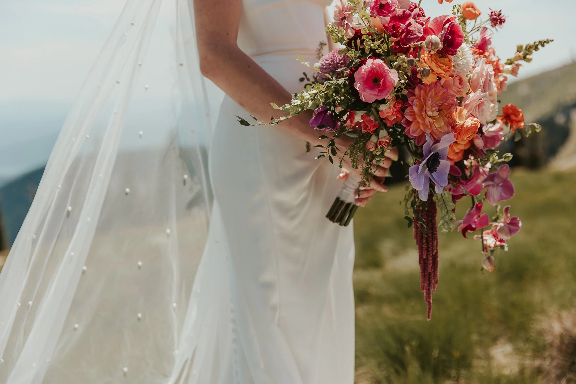Bride in a beaded white wedding dress holding a colorful floral bouquet outdoors