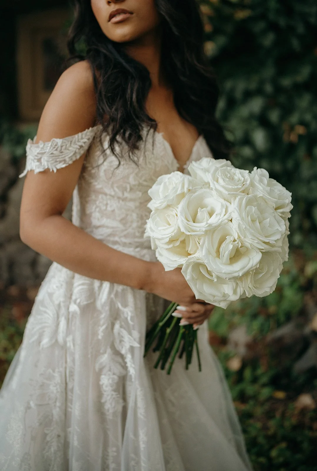 Bride in a lace wedding dress holding a bouquet of white roses outdoors
