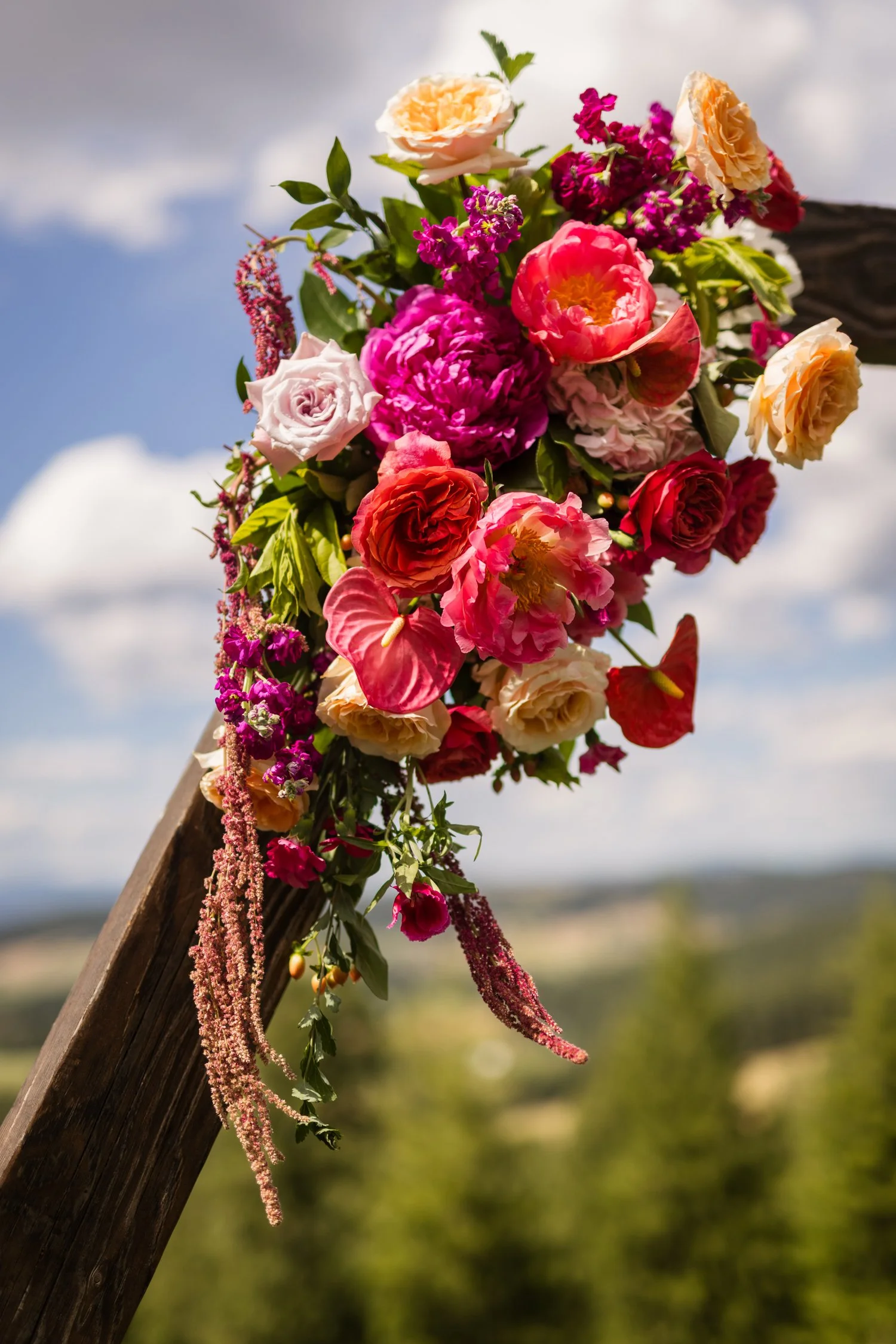 Colorful bouquet of roses, peonies, anthuriums, and trailing flowers on a rustic wooden structure outdoors