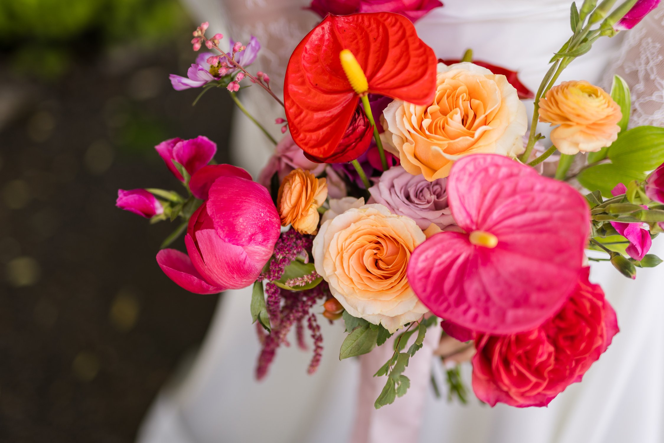 Colorful floral bouquet featuring red anthuriums, peach roses, pink flowers, and greenery