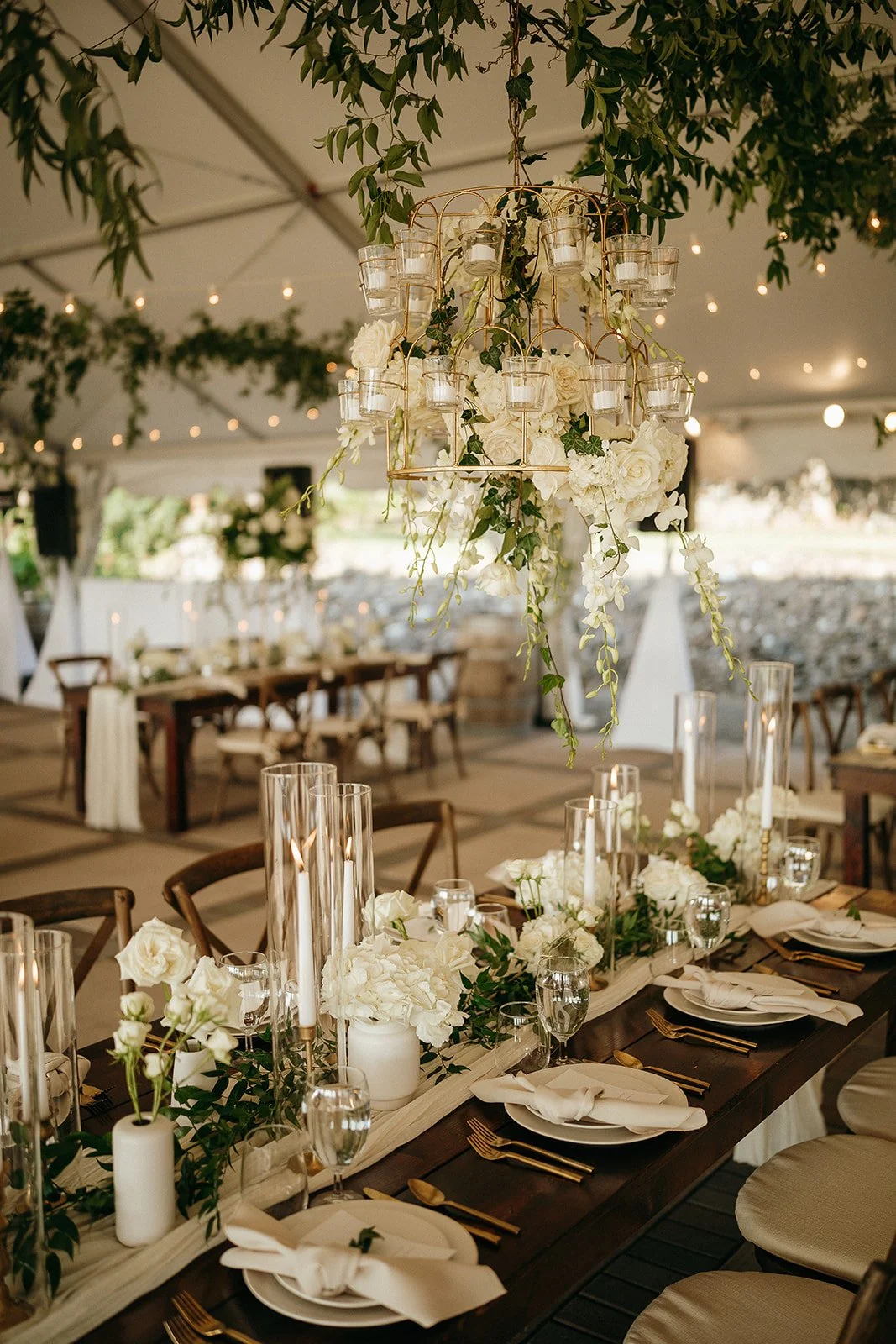 Elegant wedding reception table with white flowers, candles, gold flatware, and hanging floral candle chandelier