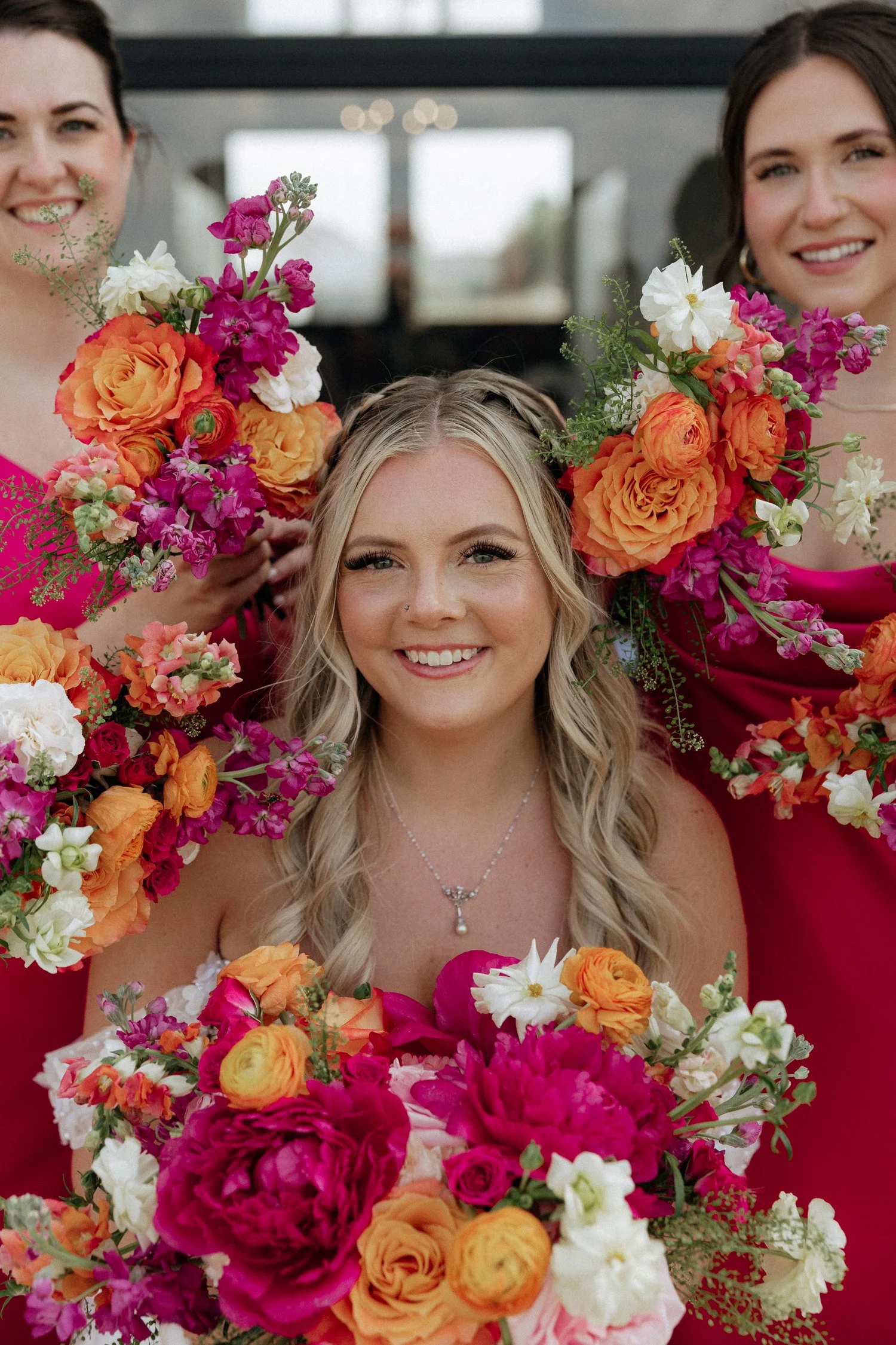 Smiling bride and two bridesmaids surrounded by vibrant orange, pink, red, and white flowers