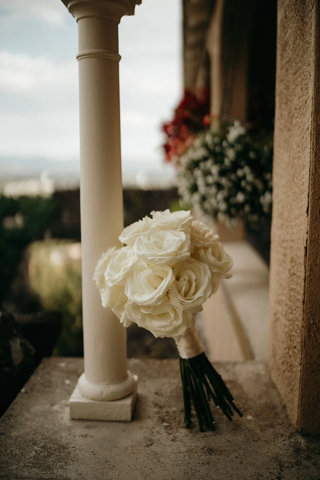 White rose bouquet beside a classical stone column on a terrace