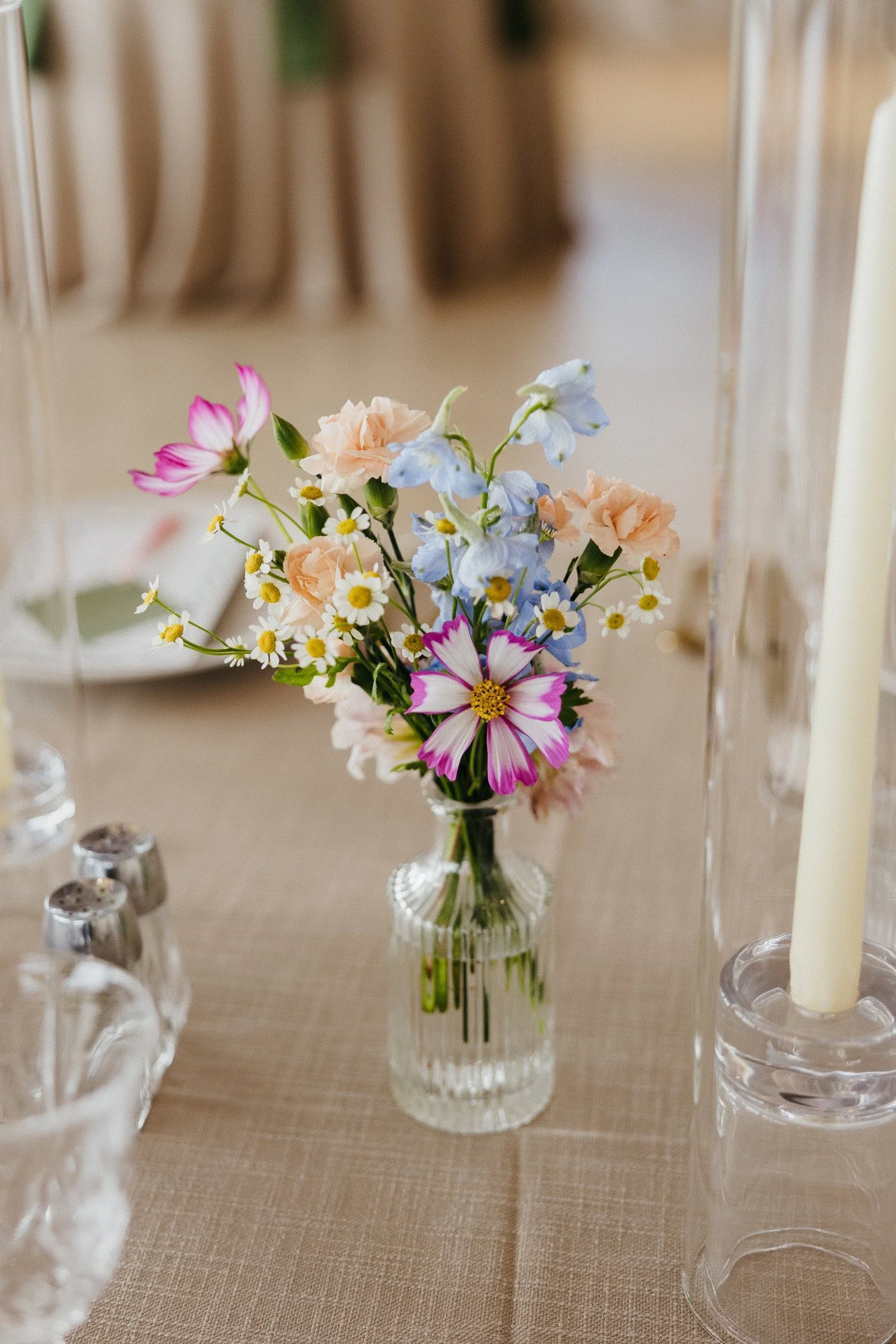 Colorful wildflower bouquet in a glass vase on a dining table beside candles