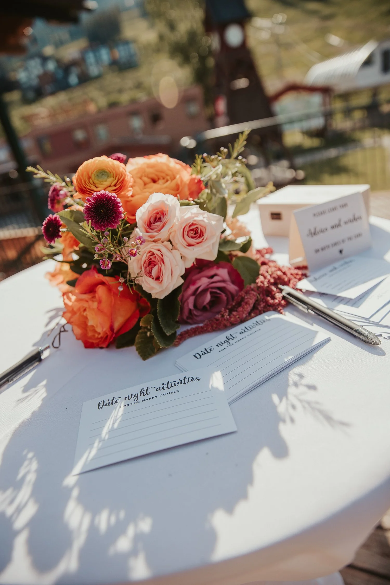 Colorful wedding bouquet beside date-night activity cards and pens on a sunlit table