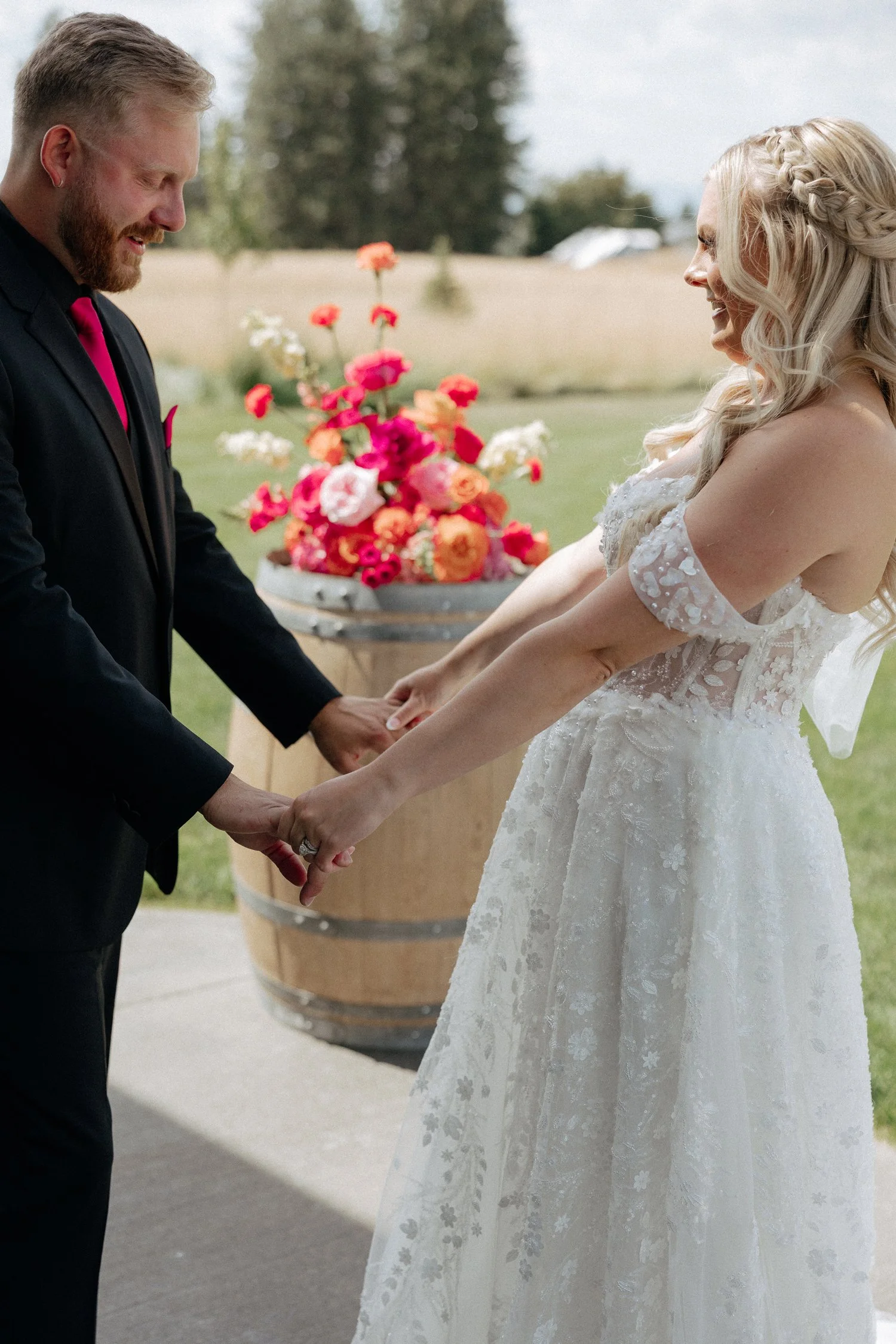 Bride and groom holding hands outdoors at a wedding ceremony beside a colorful floral arrangement