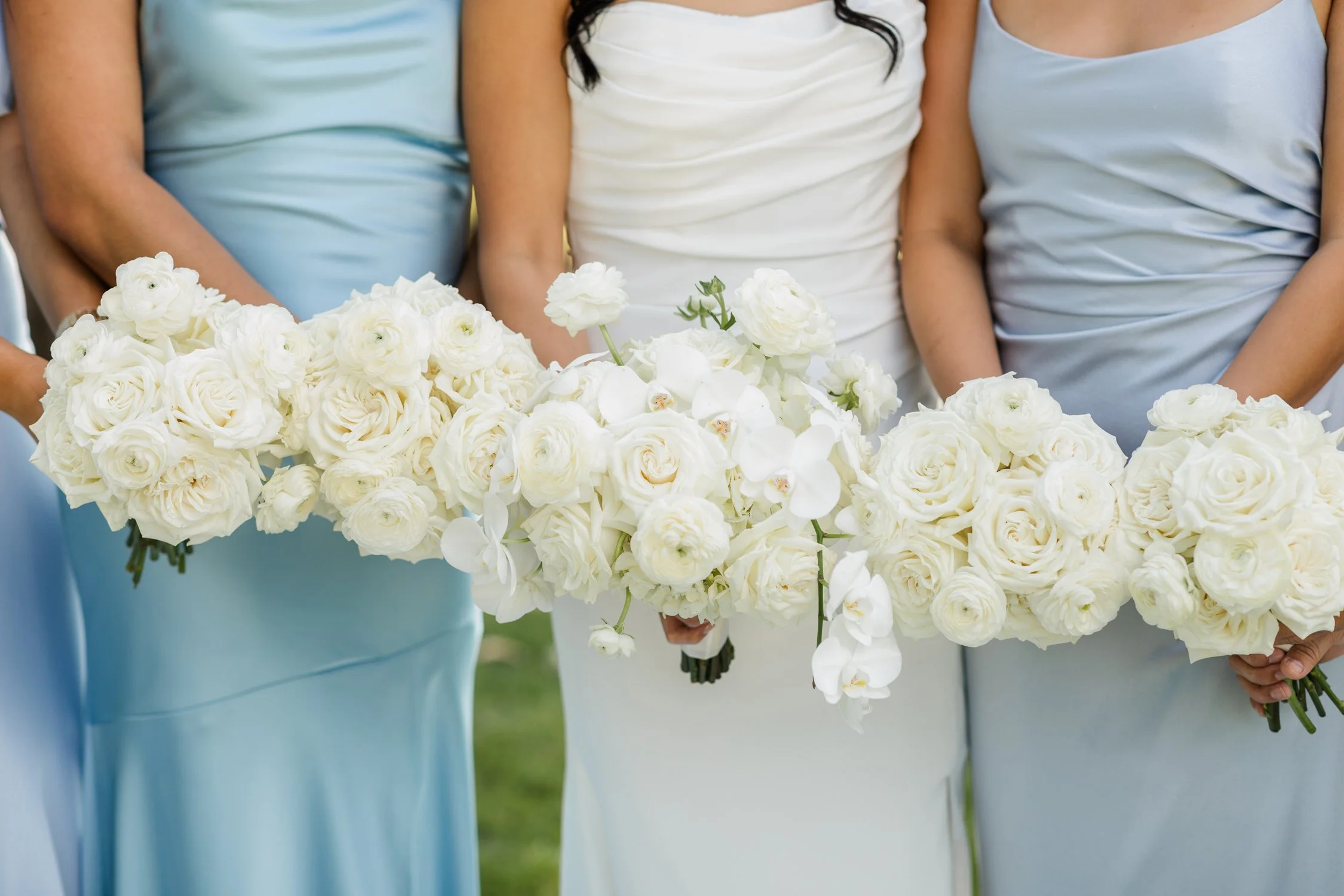 Bride and bridesmaids in white and light blue dresses holding lush white flower bouquets