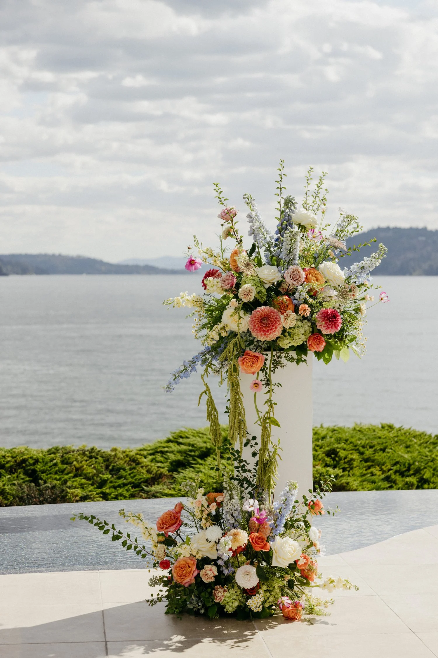Colorful floral wedding arrangement on a white pedestal overlooking a lake and forested mountains