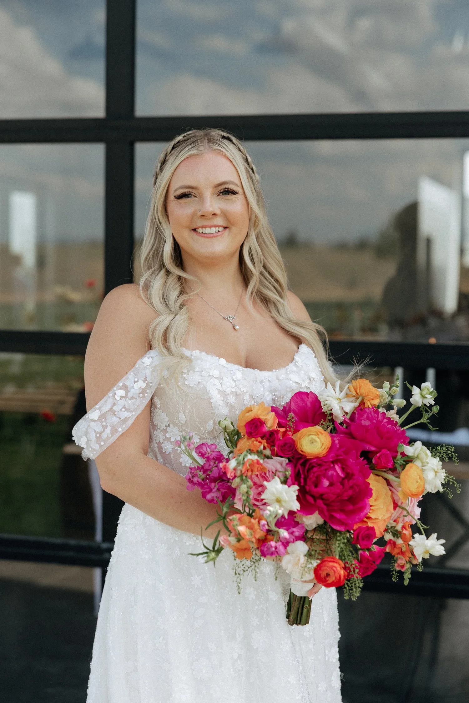 Smiling bride in a white floral wedding dress holding a vibrant pink, orange, and white bouquet