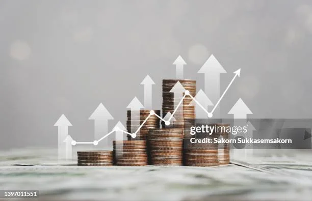 Stacks of coins with upward pointing arrows and chart overlay, symbolizing financial growth.