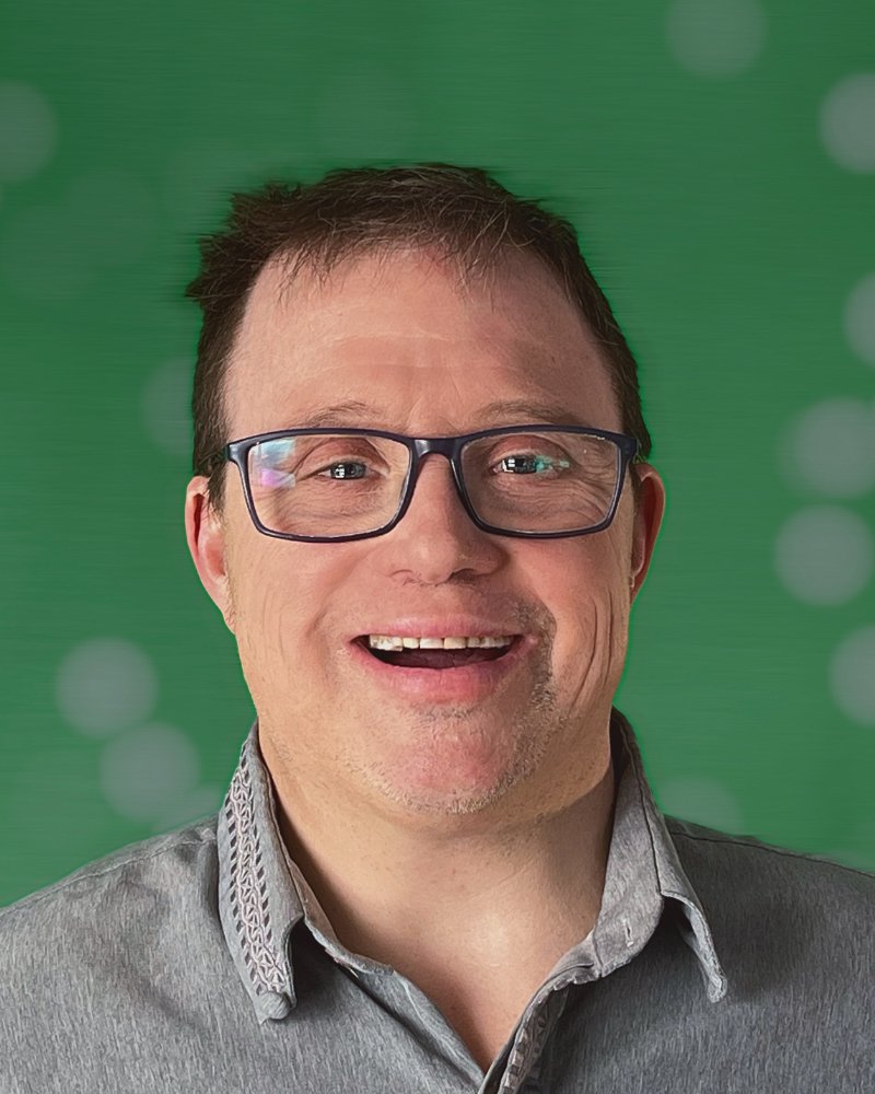 Andreas is a white man with short dark hair who wears square black glasses, and is standing in front of a green wall.
